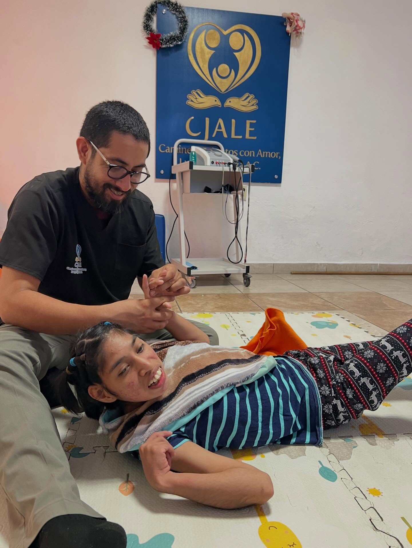 Young male teacher speaking to studying boy in school while sitting on floor in corridor. Man working with a child while discussing about examination doubts. Young and friendly teacher speaking to boy in school hallway while helping him in studies.
