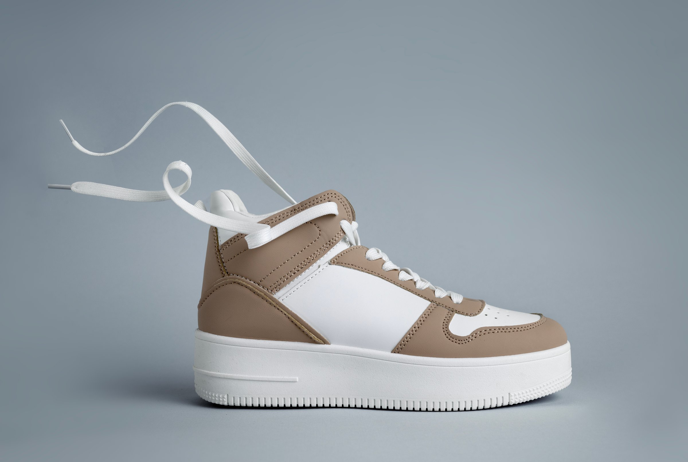 White brown sneacker closeup.Fashion shoe, leather womens sneakers isolated on gray background. Fashionable stylish sports casual shoes, minimalistic layout with footwear, shoe store advertisement.