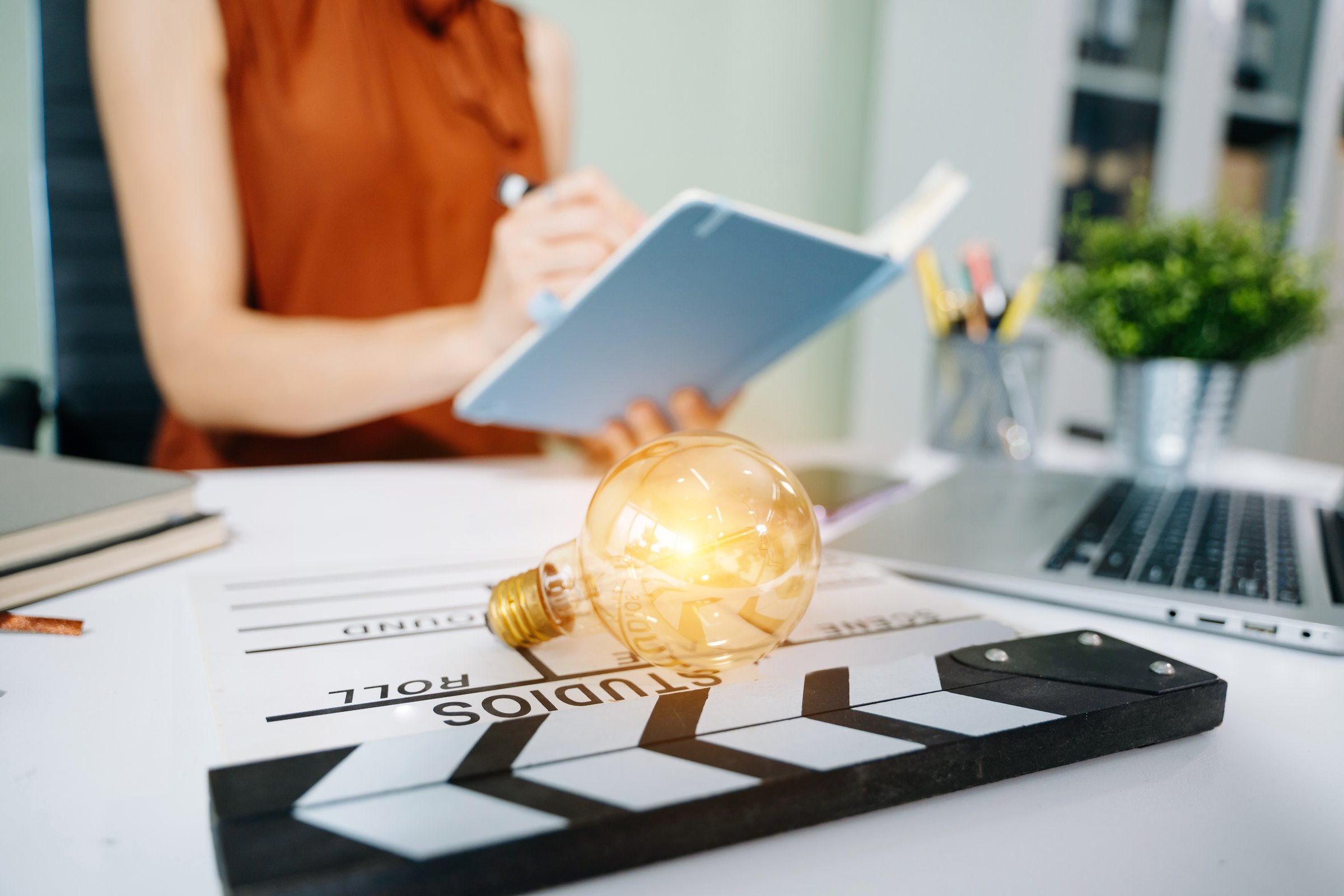 Creative film production setup with lightbulb and clapperboard on desk, symbolizing innovation, inspiration, and storytelling ideas in a modern digital workspace.