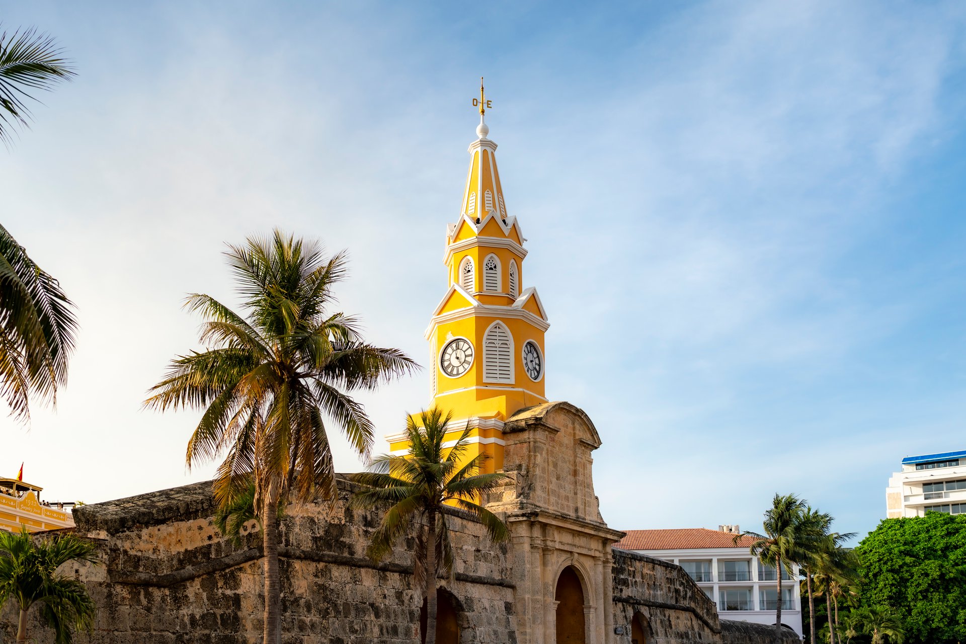 Famous yellow clock tower Torre del Reloj stands tall in Cartagena, Colombia, surrounded by tropical palm trees and colonial walls.