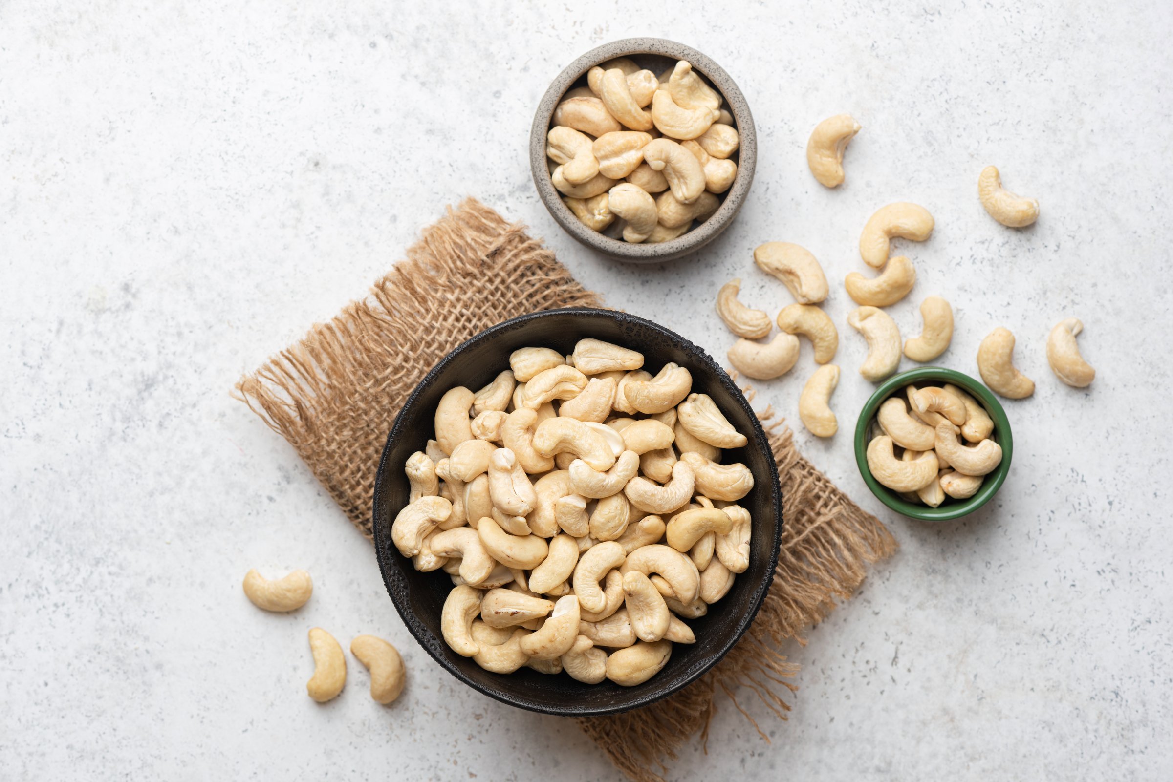 Peeled dry cashew nuts in bowl on grey background, table top view