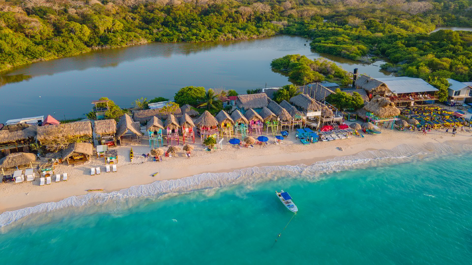Stunning aerial shot of Playa Blanca, featuring colorful beach huts, crystal clear waters, and lush greenery in Cartagena, Colombia.