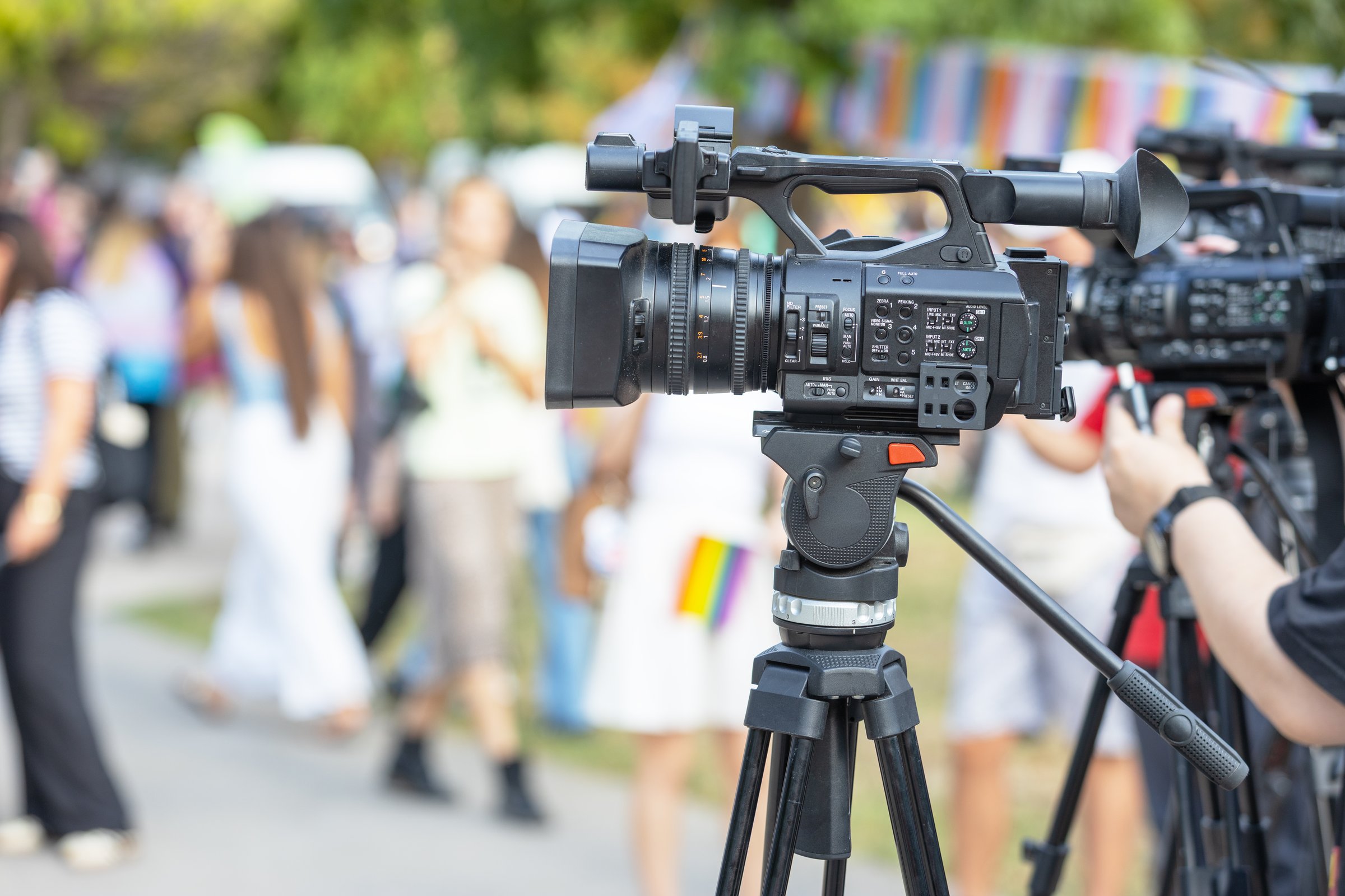 Professional video camera recording outdoor event with people in background, journalism, broadcasting, media coverage, television production, live reporting, press coverage and communication concept