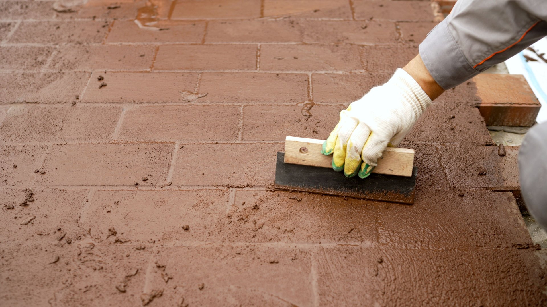 Construction worker spreads grout between bricks on a pathway, ensuring stability and a polished finish