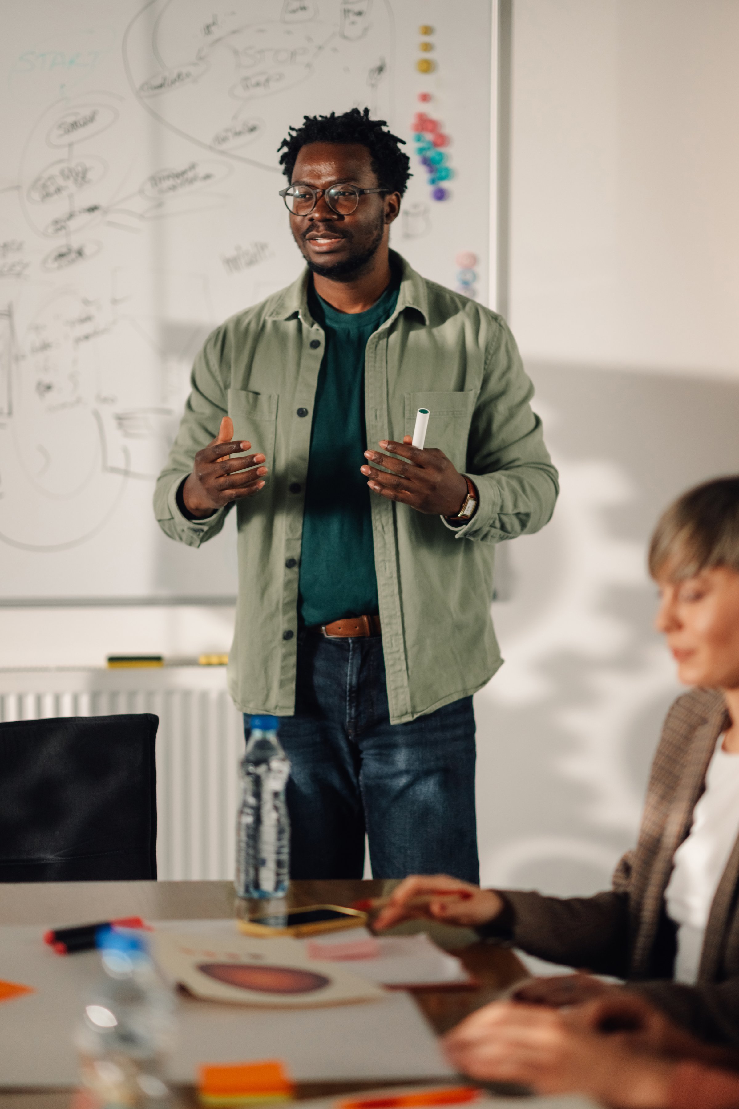 Confident young african american male professor explaining a new lesson to his students while standing near whiteboard in university classroom