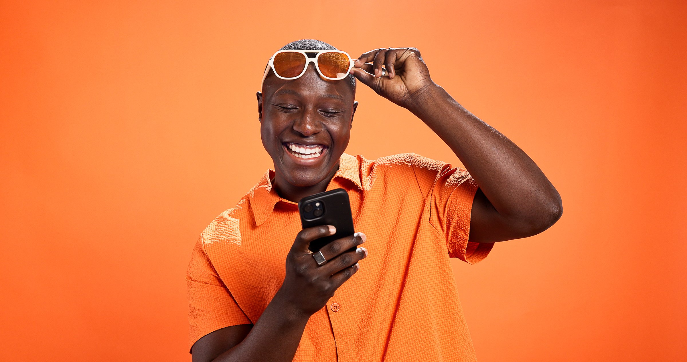 Excited, fashion or black man with phone in studio for surprise discount, sale or bargain deal. Space, notification or happy model on orange background in trendy sunglasses, good news or cool clothes