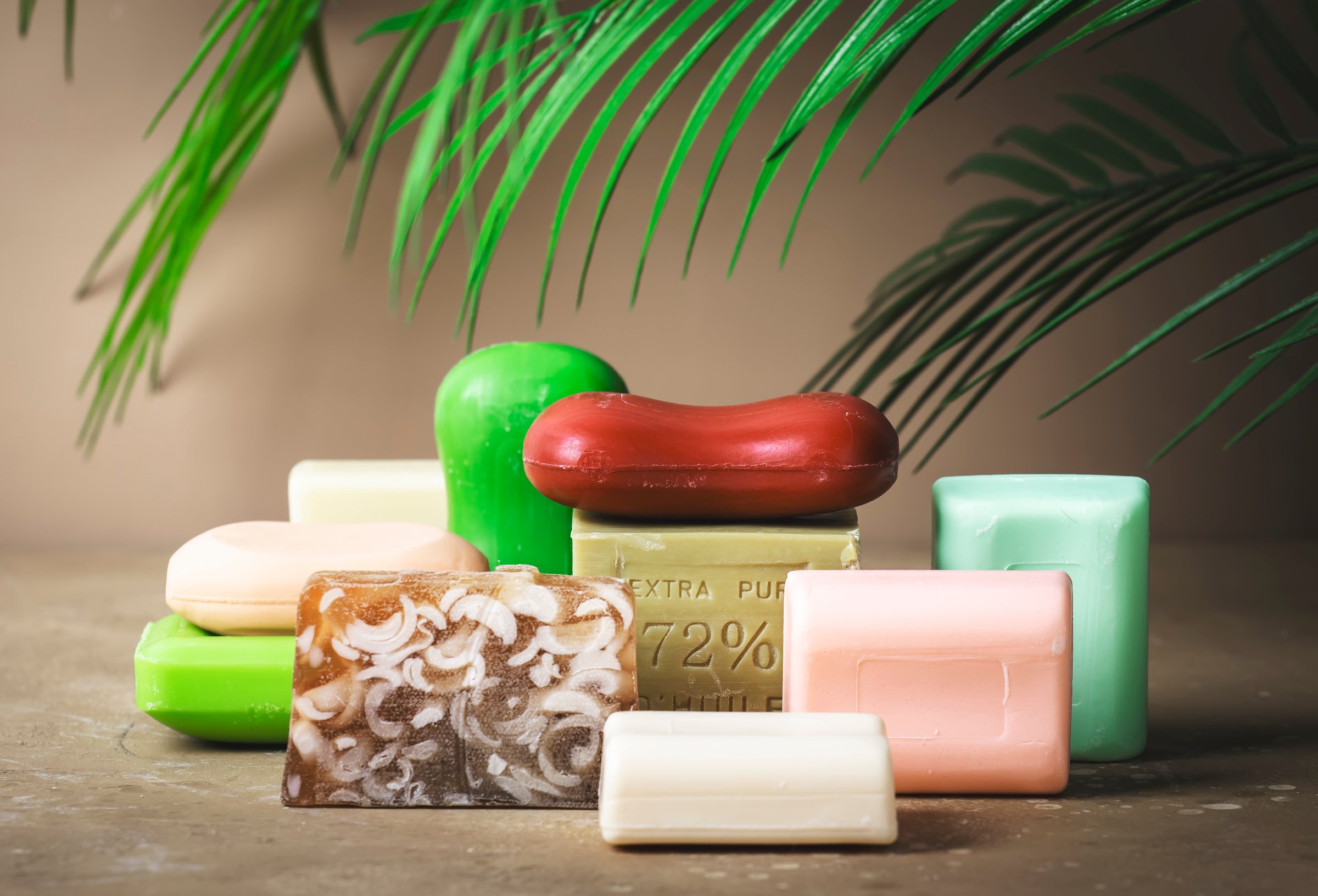 Assortment of solid toilet moisturizing soap on beige background. Hard light, leaves, shadows
