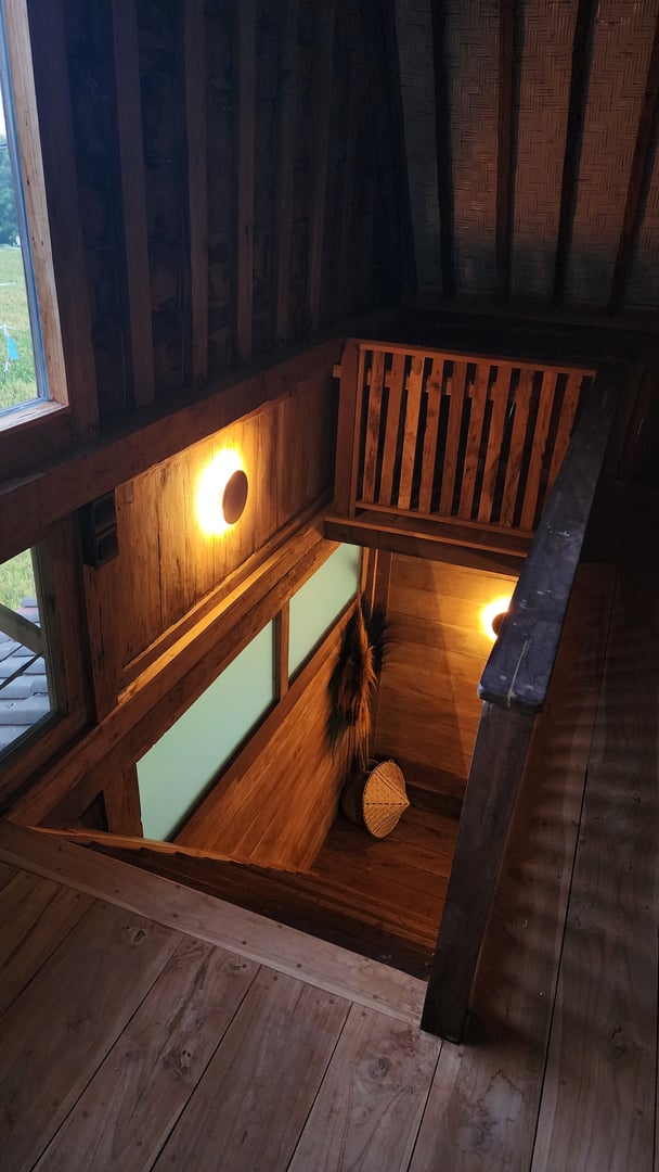 A rustic wooden staircase with dim wall lights, leading down to a lower level with a woven basket and decorative items.