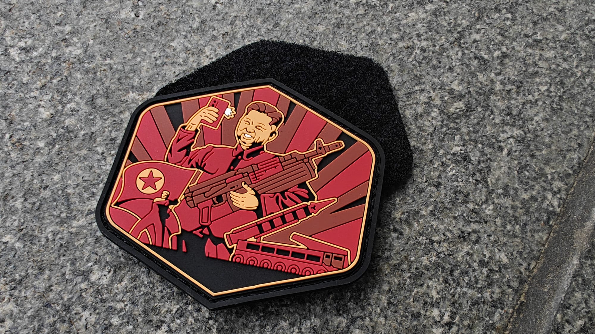 Patch featuring a stylized illustration of a soldier with a rifle, tank, and flag on a gray surface.
