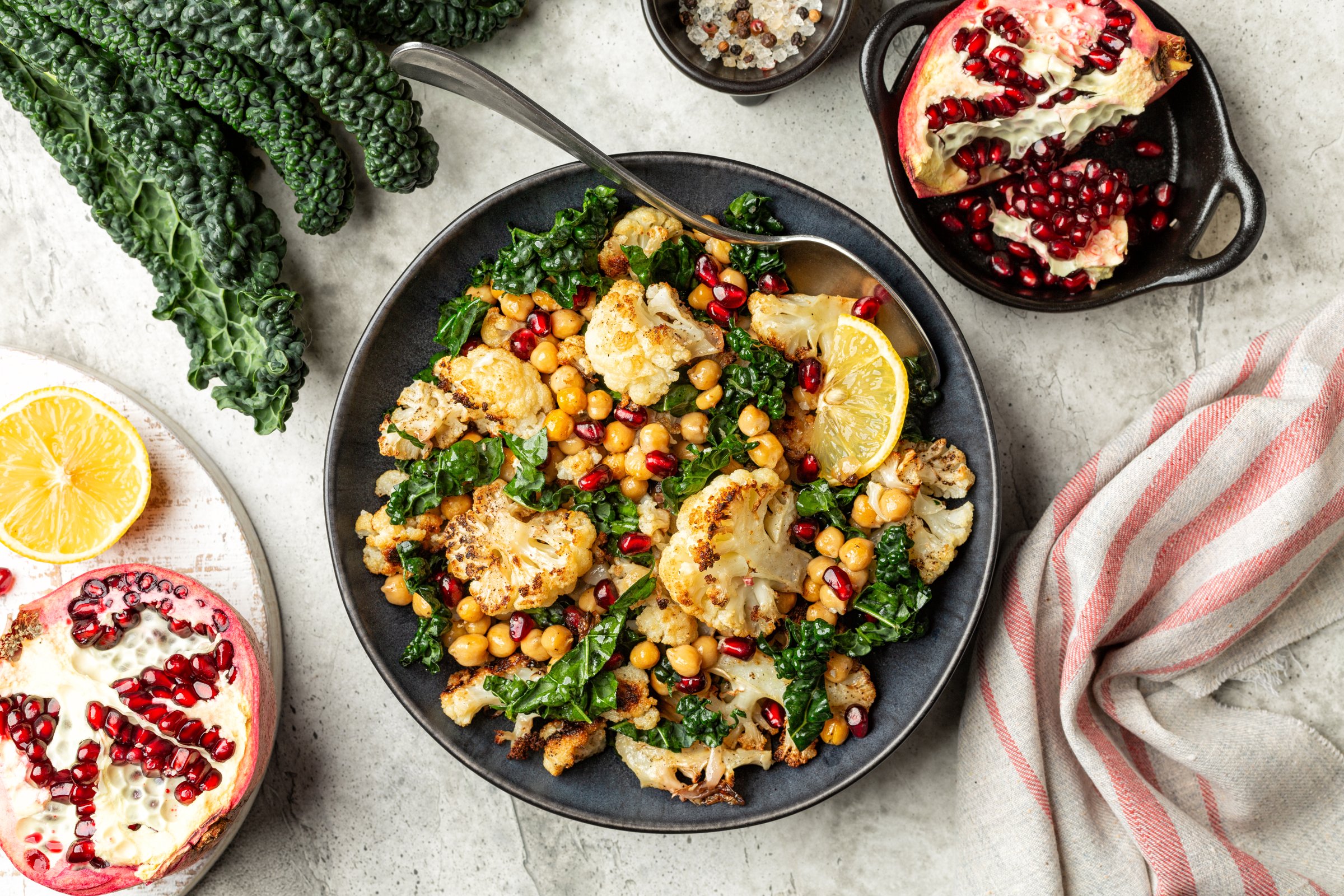 Roasted Cauliflower and roasted chickpeas salad, with pomegranate, kale, with spices, oil and lemon dressing. Vegetable winter season food on a light background.