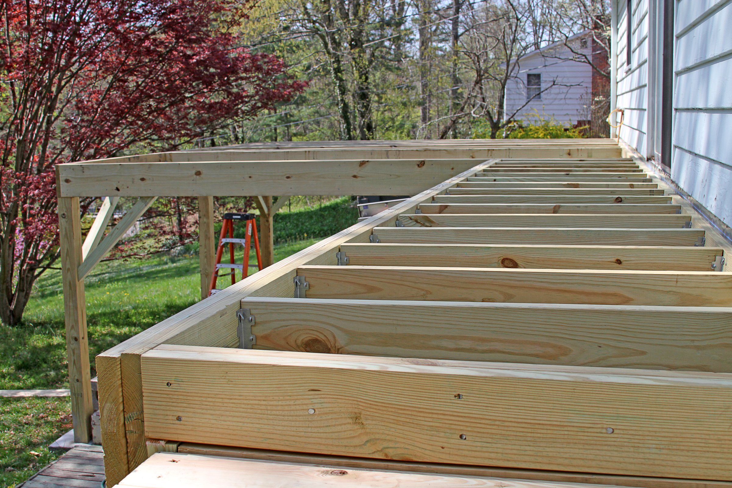 An outside wooden deck half built with slats and a ladder below