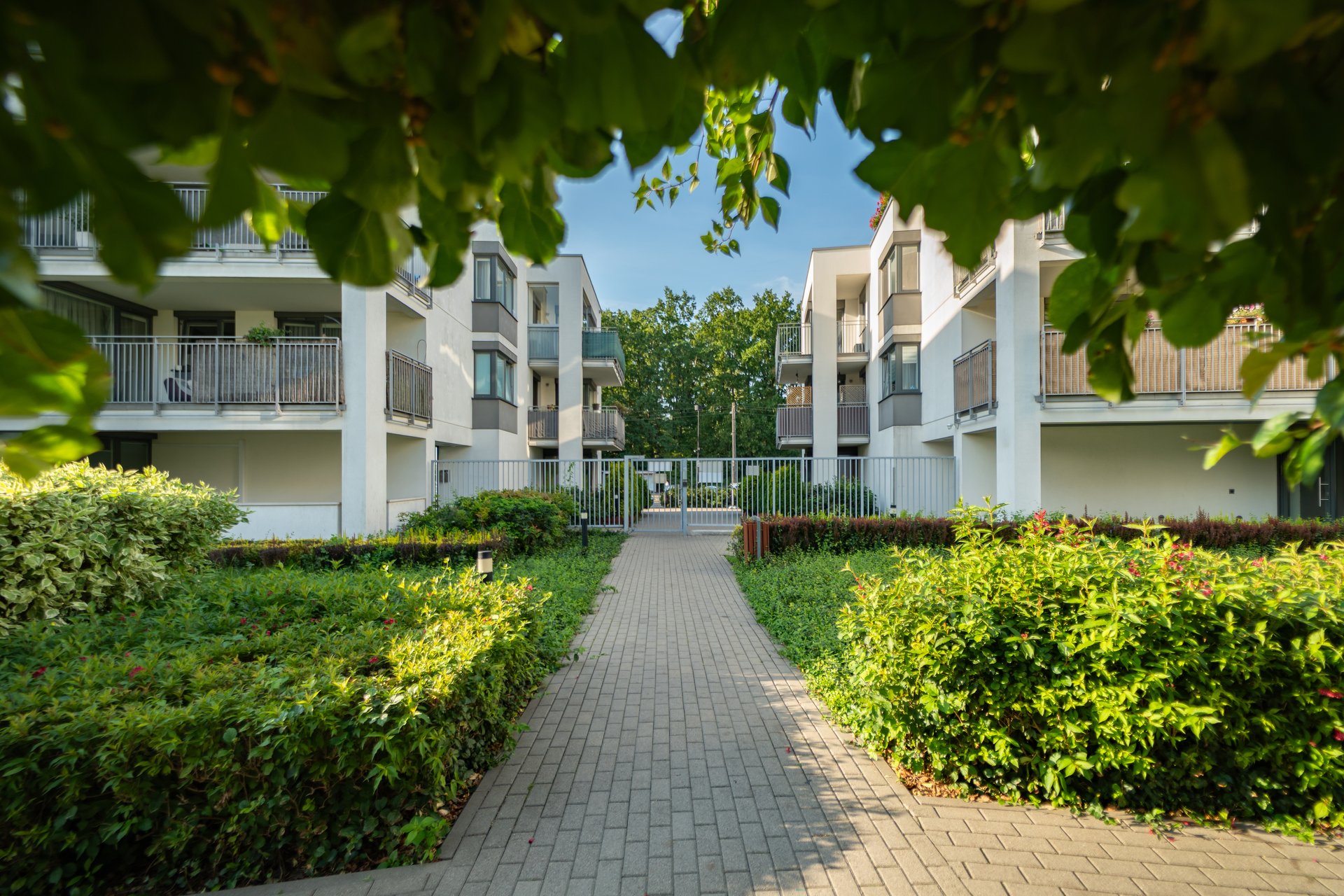 A secluded walkway inside a private residential area leads to a closed gate. The secure, gated community with apartment buildings creates a private and tranquil residential environment.