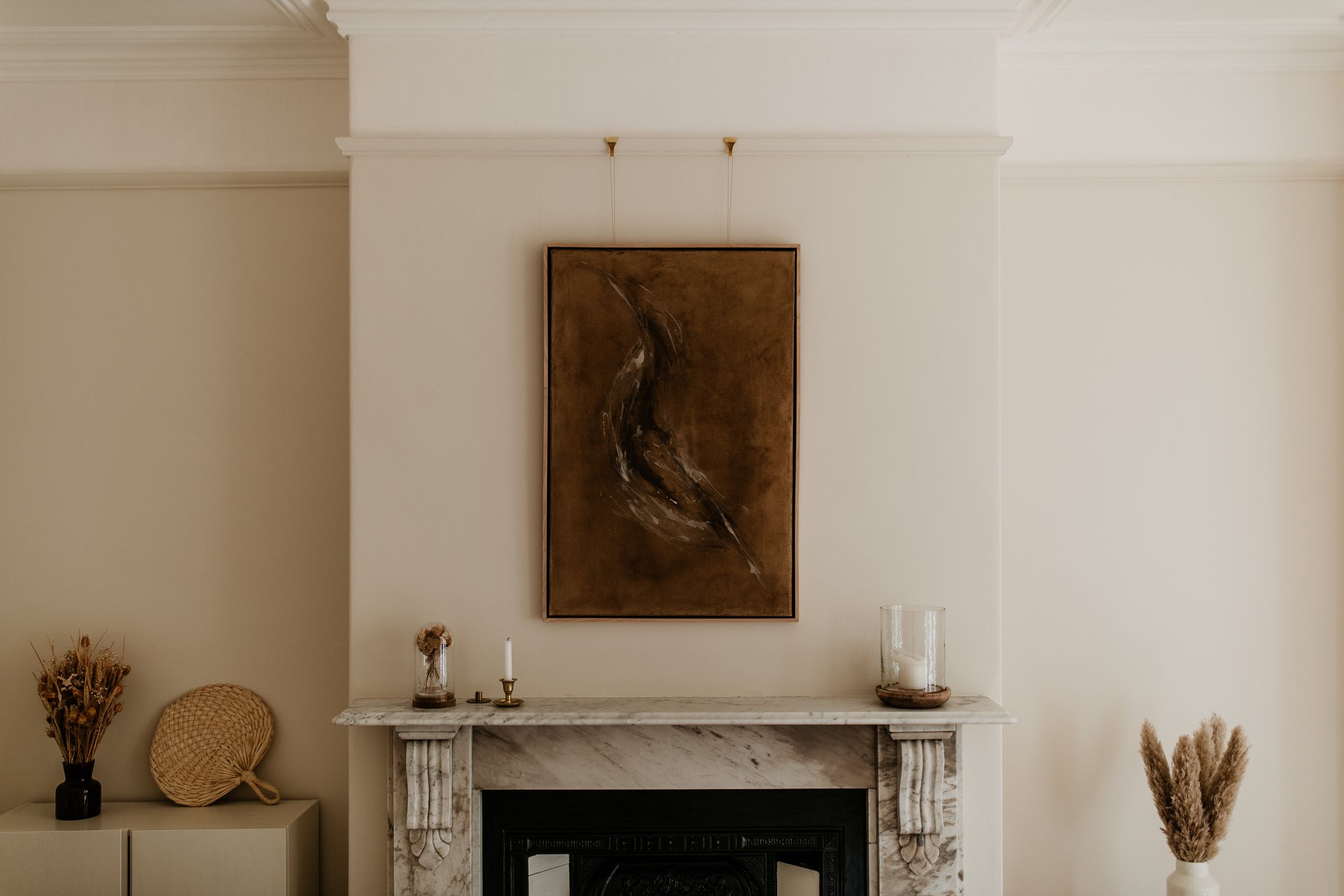 A warm minimalist interior featuring abstract wall art above a classic Victorian marble fireplace. The blend of clean lines, natural light, and historical detail creates a sophisticated yet cozy atmosphere.