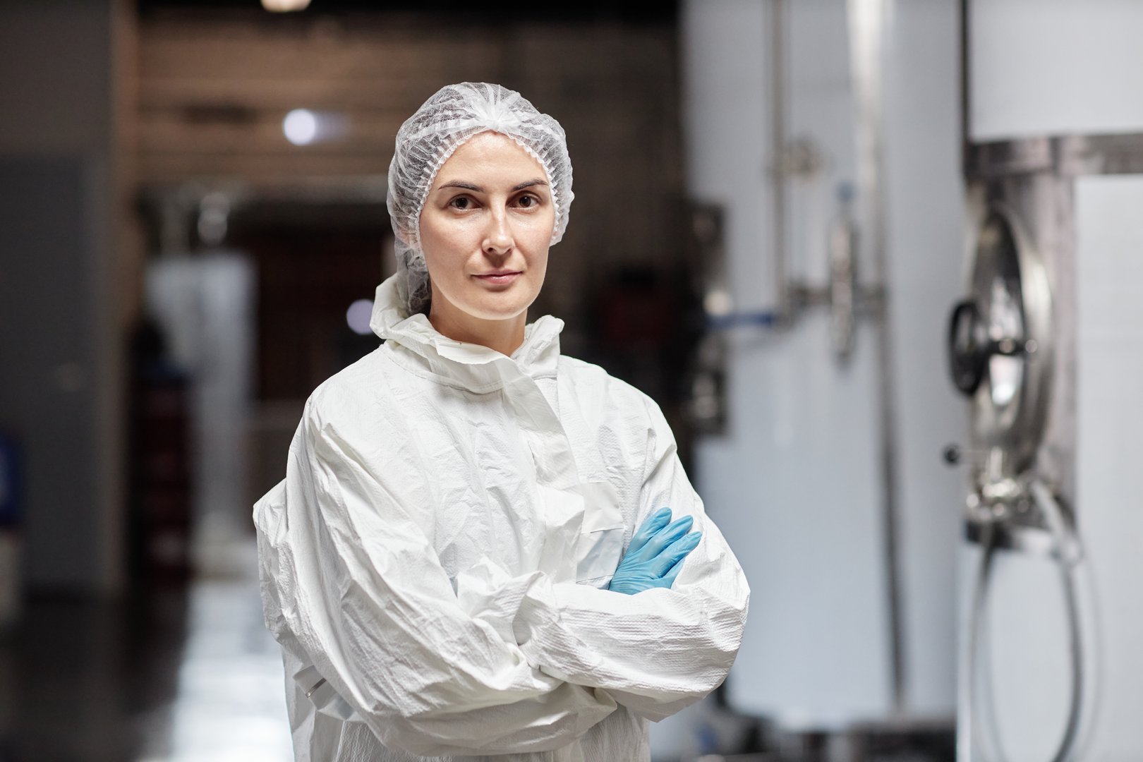 Medium portrait shot of confident female production worker in coverall posing for camera with arms crossed in workshop at factory, copy space