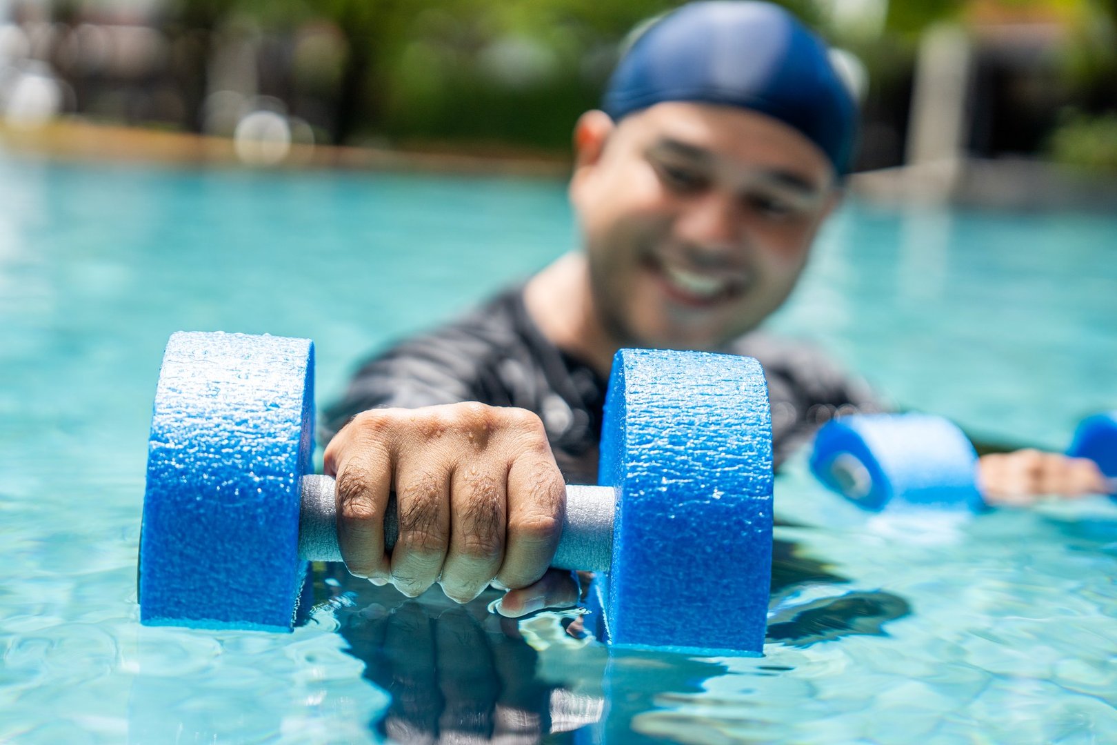 A smiling person in a swim cap and rash guard is submerged in a pool