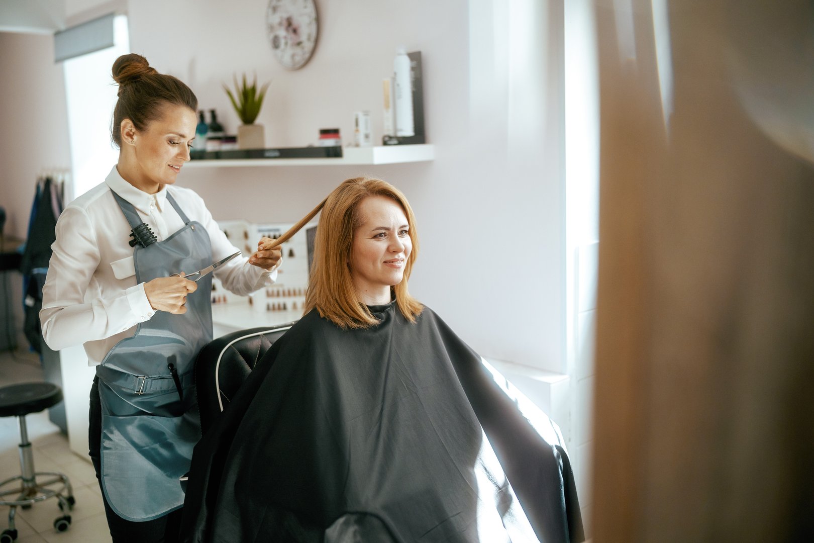 middle aged woman hairdresser in modern hair studio with scissors and client cutting hair.