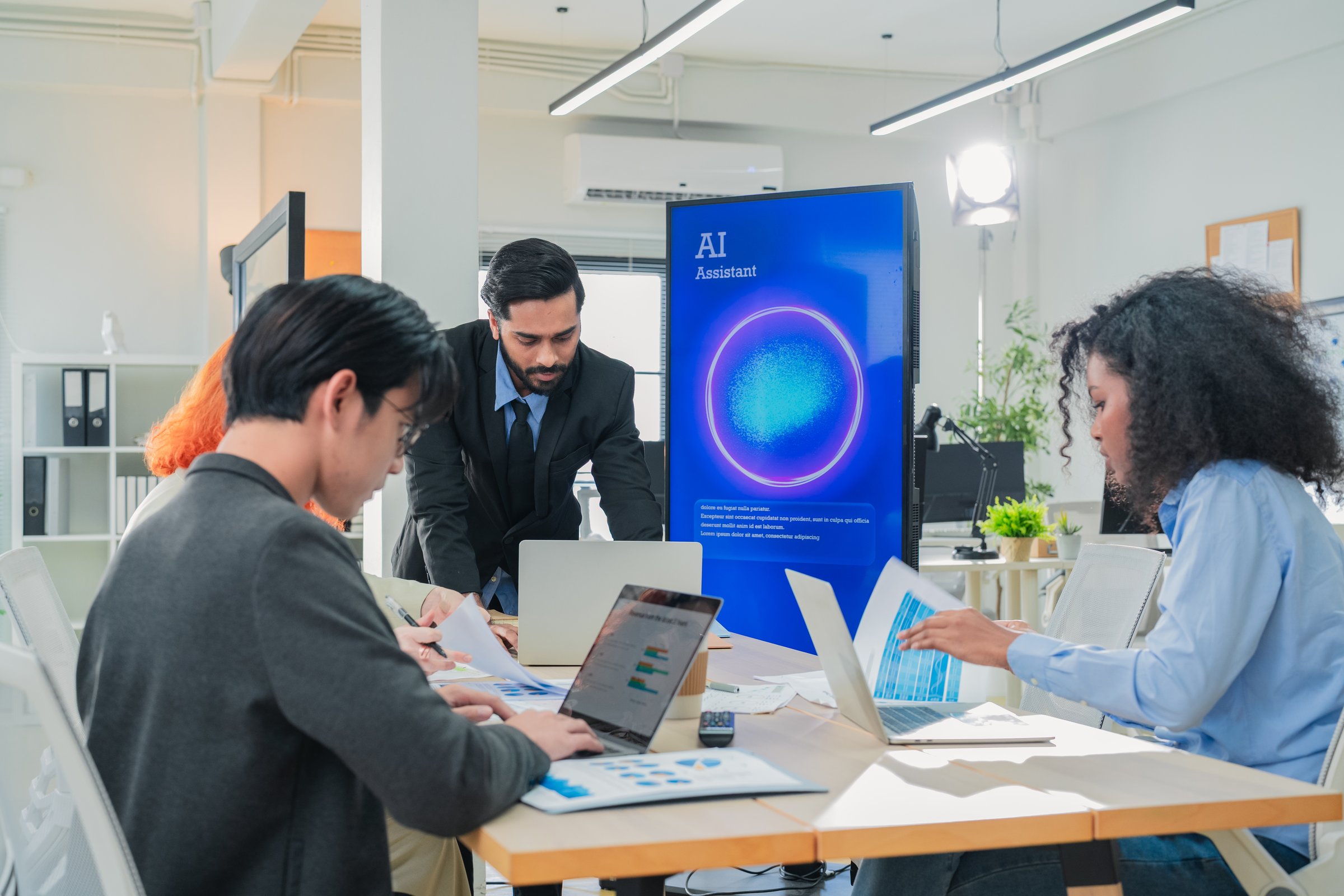 Diverse business professionals meet in bright office interior, using AI virtual assistant to brainstorm
