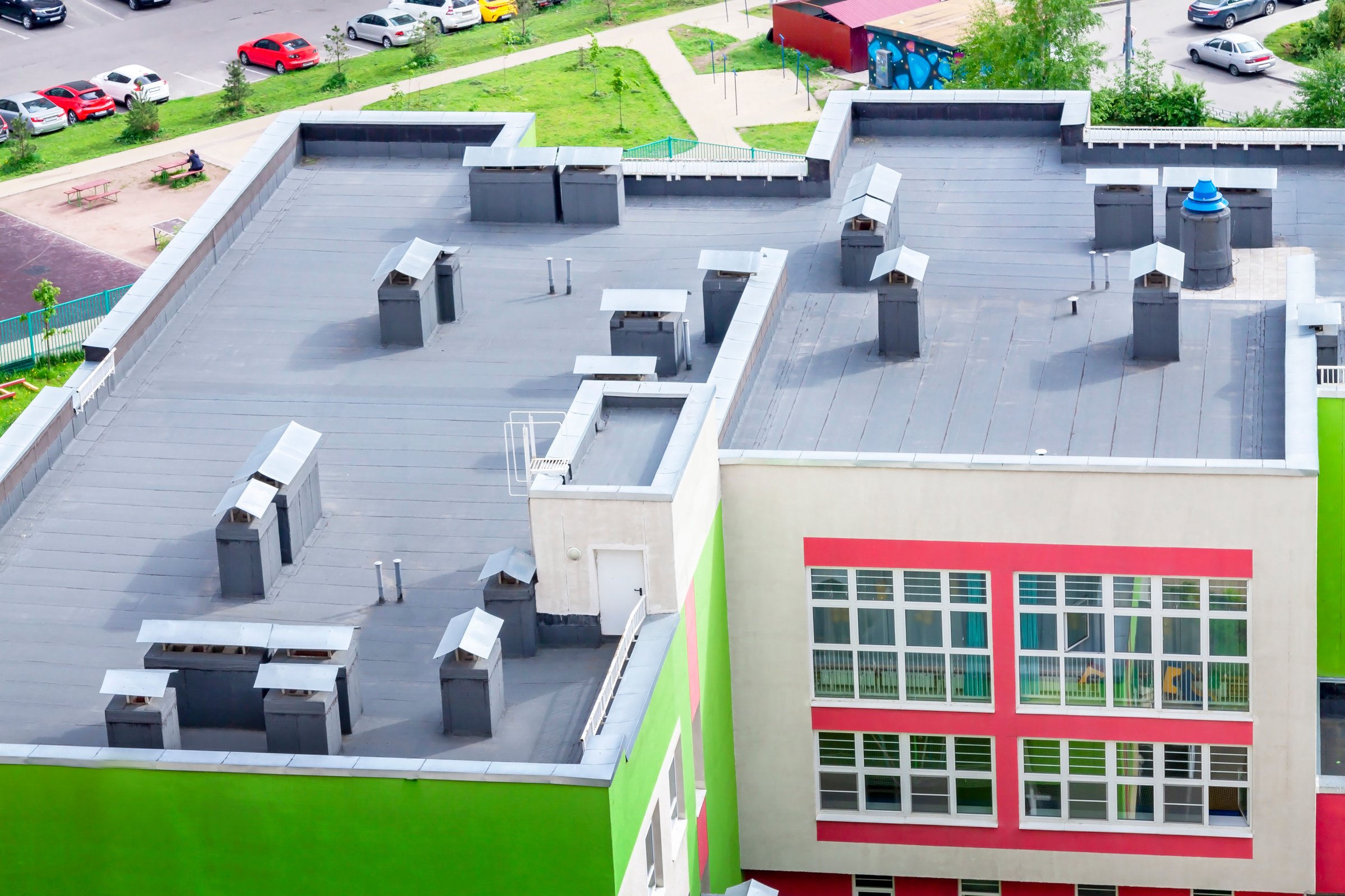Top view flat roof with air conditioners and hydro insulation membranes on top of a modern school green red building. Back to school concept.