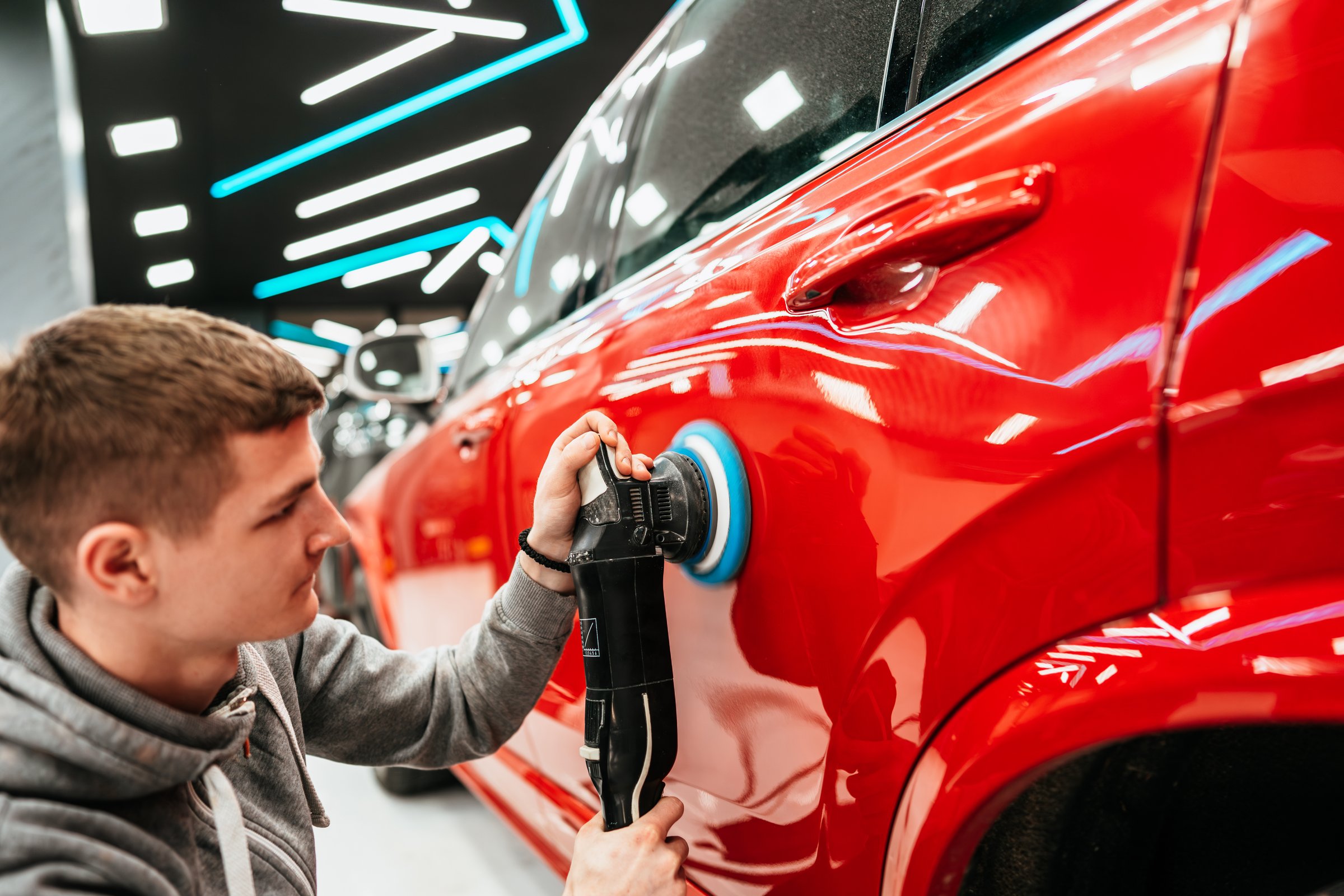 Professional vehicle polishing and detailing service in a modern car workshop. Brightly lit workspace with large led lights. High quality car valeting concept.