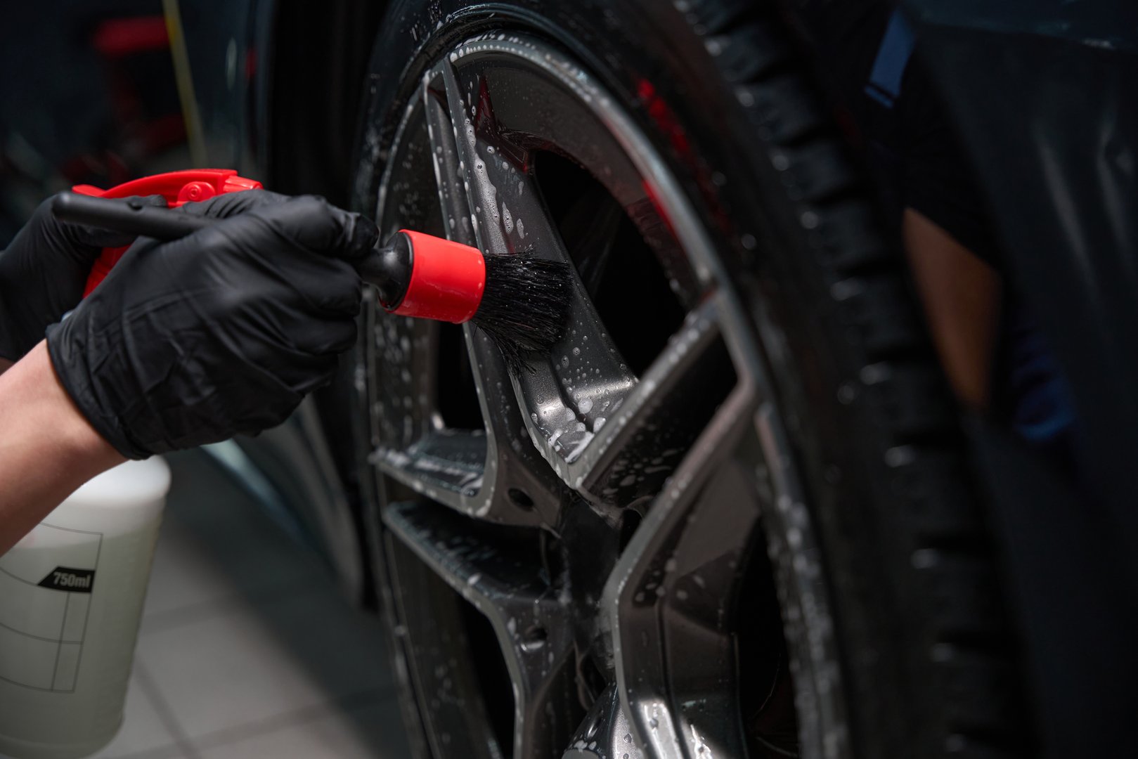 Closeup of male hands in nitrile gloves cleaning car wheel spokes with cleaner and brush