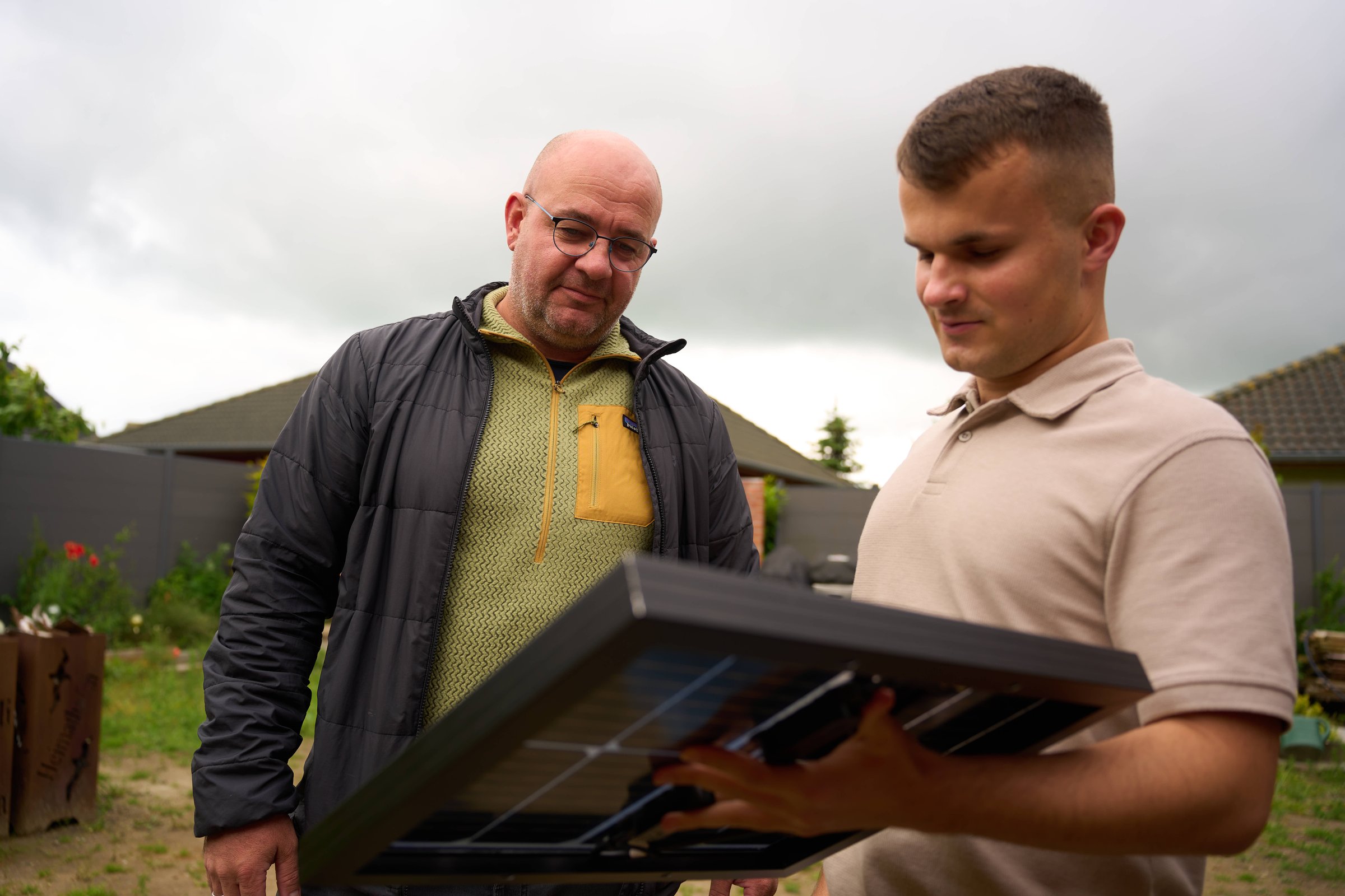 Two men examining a solar panel outdoors, one holding it and showing it to the other.