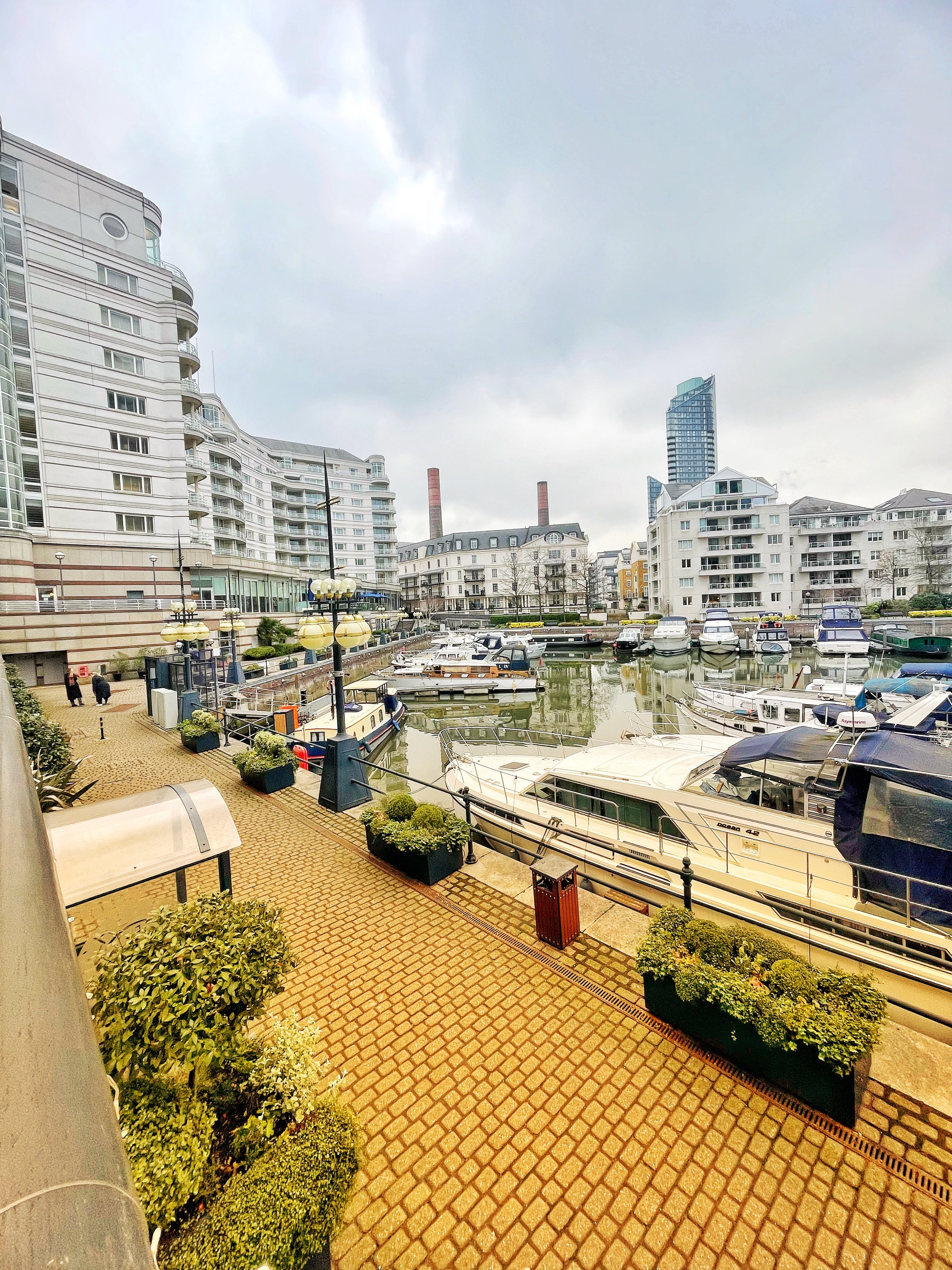 Marina with docked boats, surrounded by modern residential buildings and cloudy sky in an urban setting.