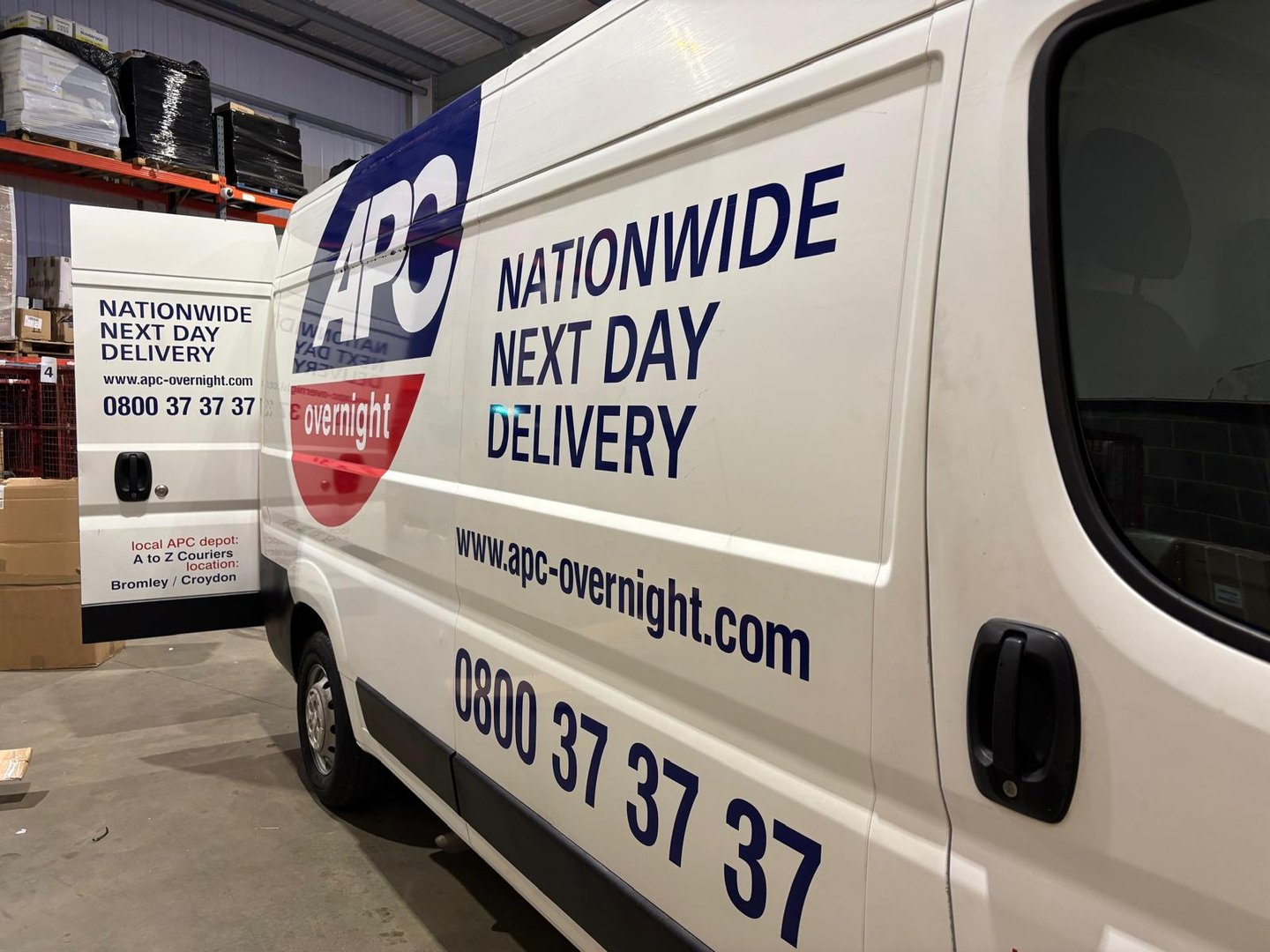 A delivery van with APC Overnight branding, featuring slogans for nationwide next day delivery and a contact number.
