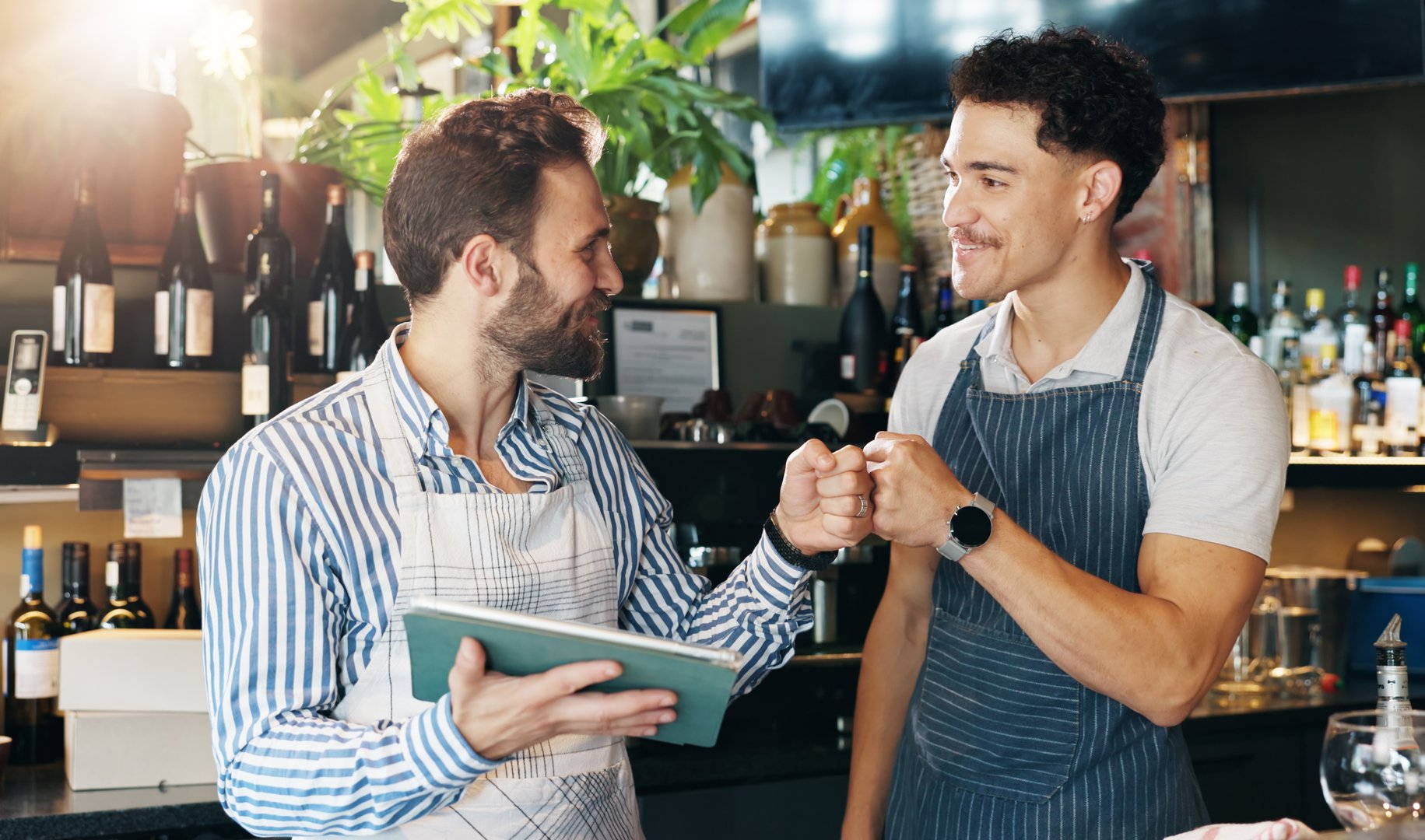 Waiter, team and tablet in cafe with fist bump, positive online review or happy for order increase. Service industry, men or tech in restaurant for digital menu, hospitality or excited for shift list