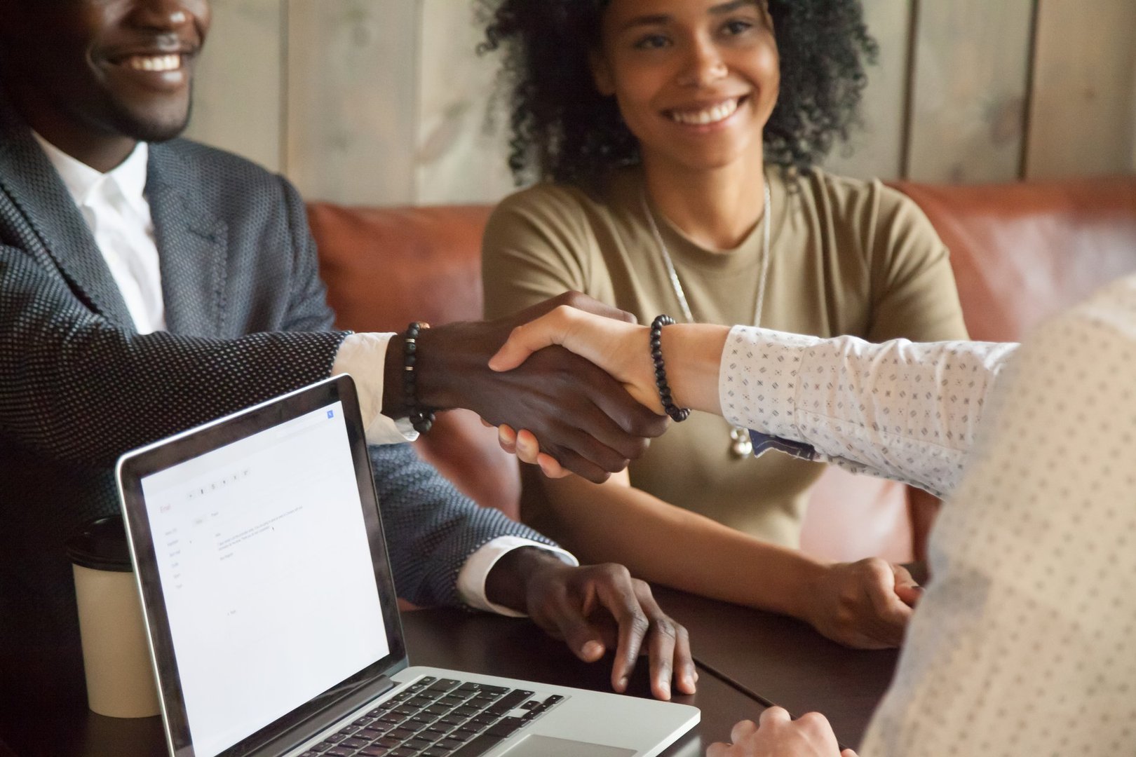 Happy young african american couple making deal handshaking caucasian insurance broker in cafe, black satisfied customer and Real Estate Agent or sales person shaking hands at meeting in office with laptop