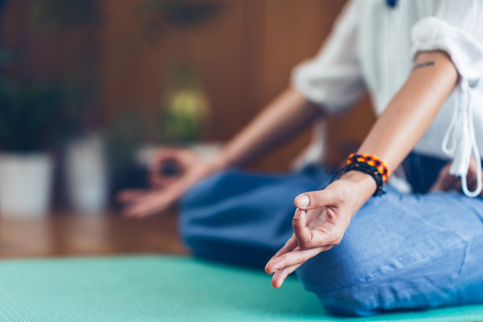 Person sitting cross-legged on a yoga mat meditating, wearing a bracelet, with hands in a mudra gesture.