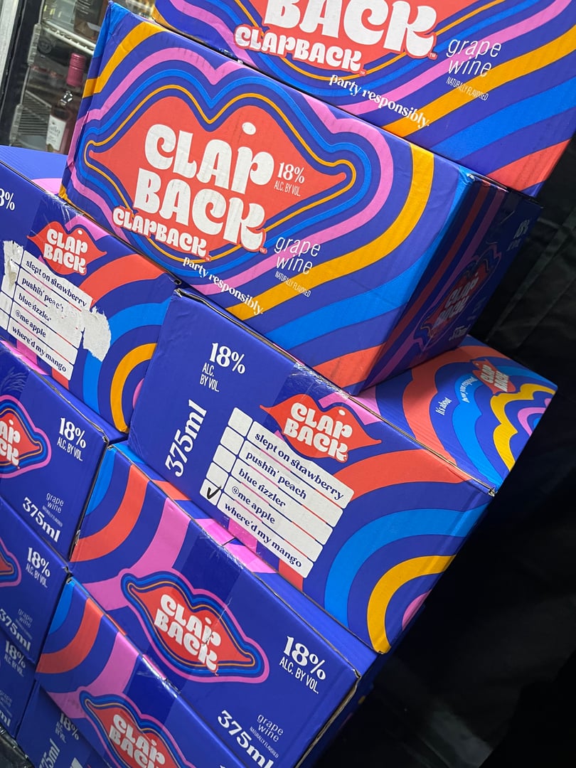 Stacked boxes of Clap Back grape wine, 18% alcohol, 375ml bottles, with colorful wave design on packaging.