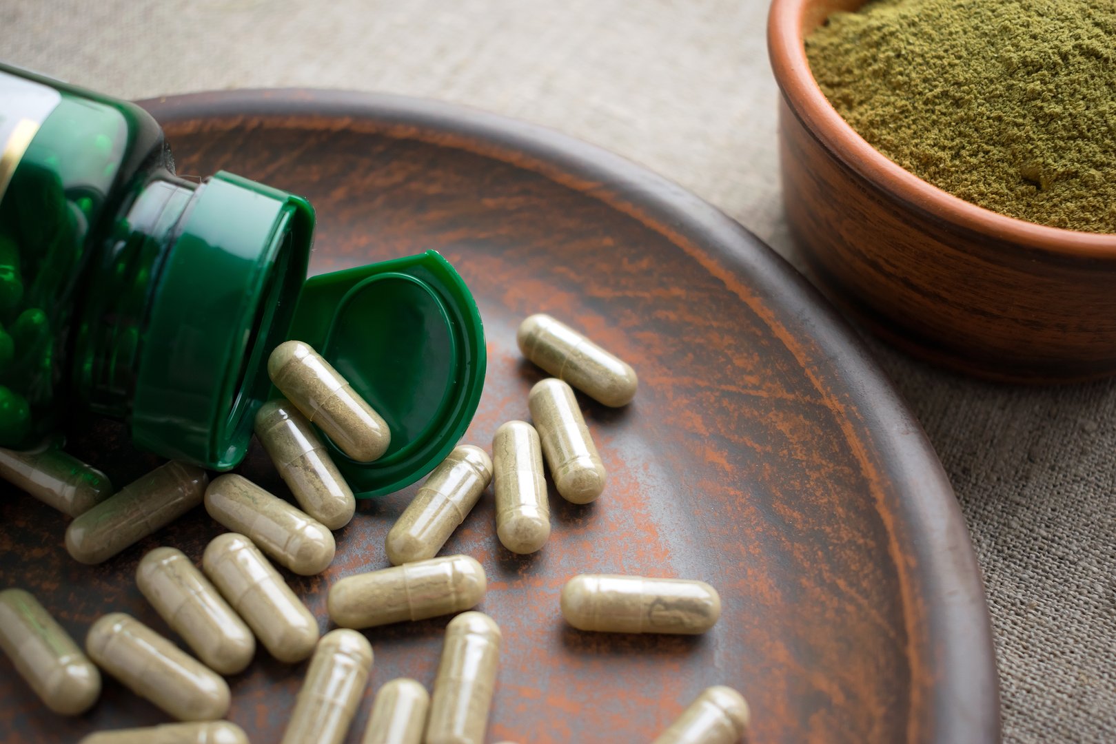 Close up Green capsules, bottle and powder on a clay brown plate