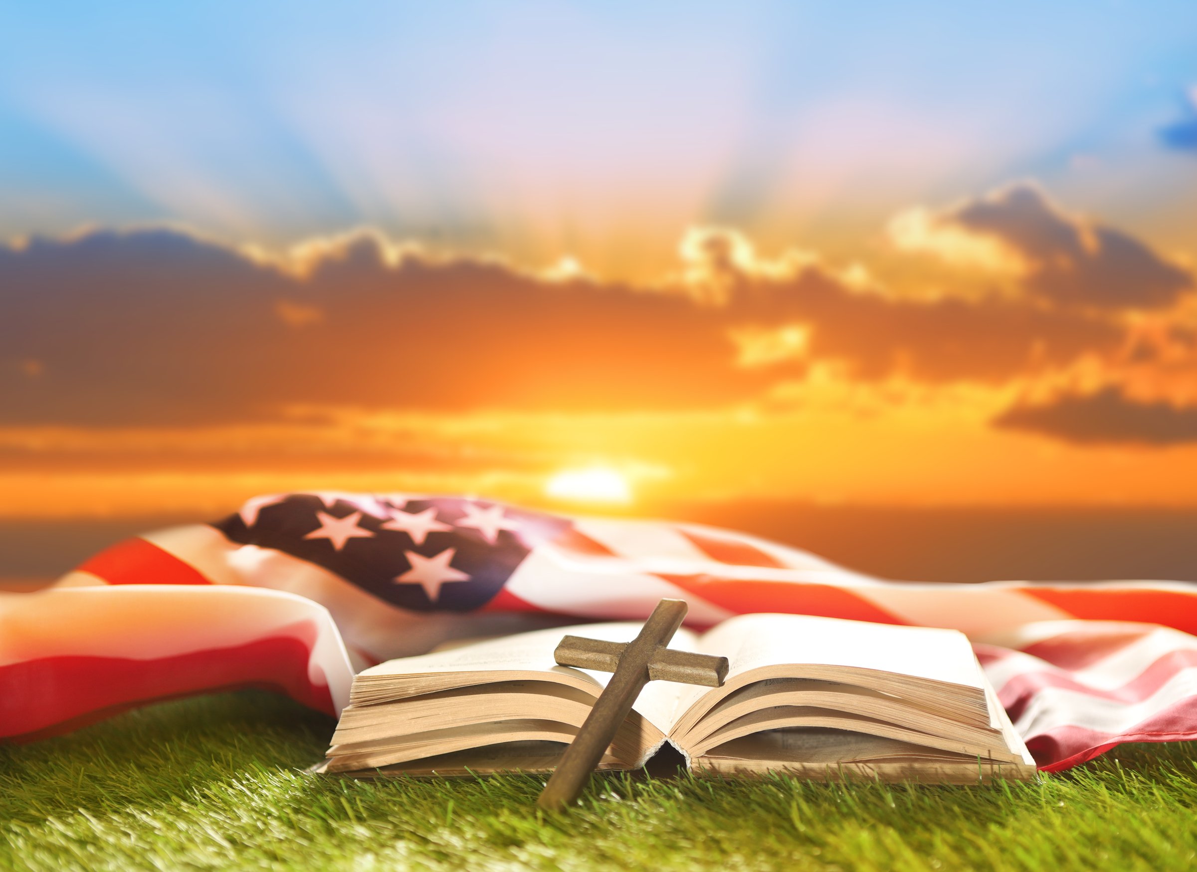 Holy Bible, Christian cross and US flag on grass. Sunny day. God Bless America