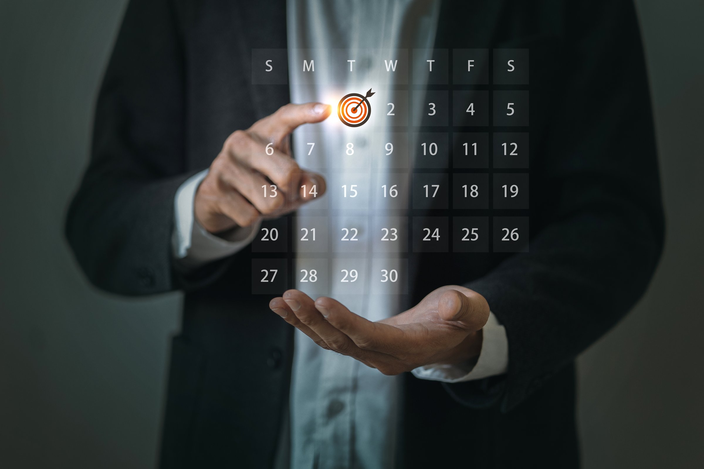 A business professional selecting a date with a target icon on a digital calendar interface floating above his hand.