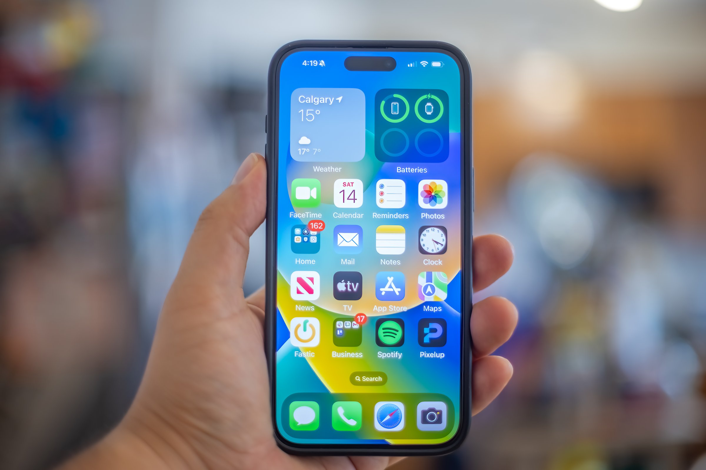 Calgary, AB, Canada. Sep 14, 2024. A hand holding an iPhone 15 Plus, Black modern smartphone displaying a customized home screen, showing various app icons and widgets, including weather.
