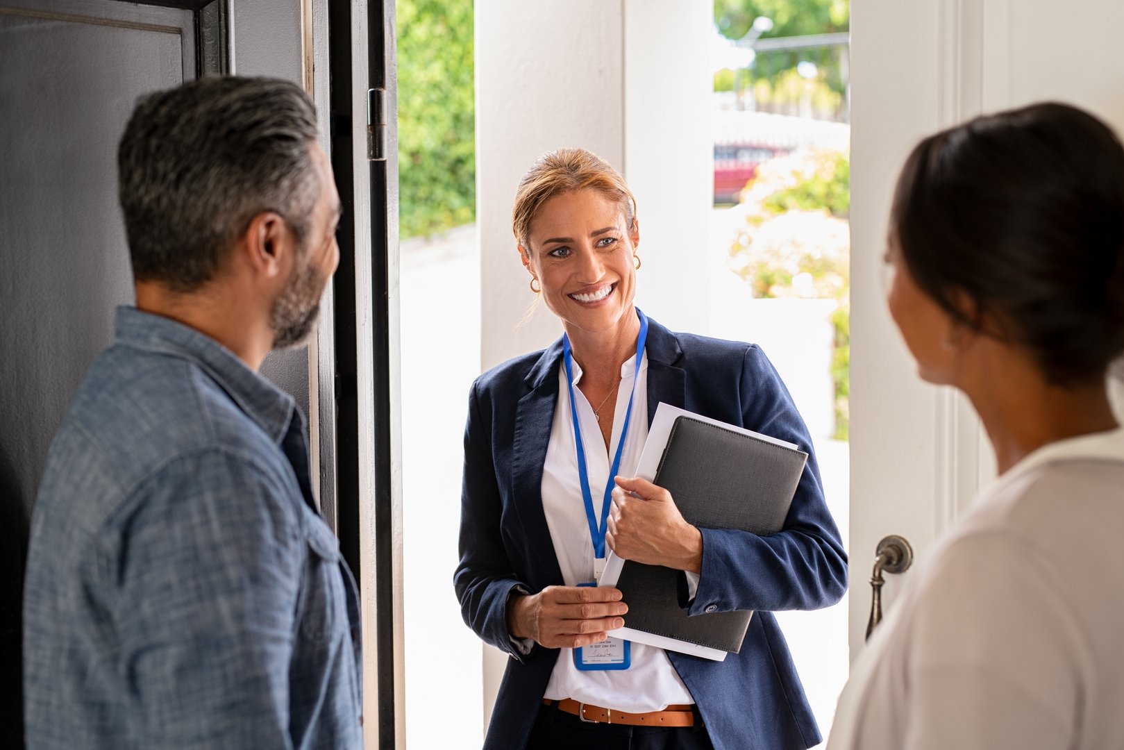 Smiling mature social counselor meeting mature couple at home. Happy multiethnic man and latin woman greeting agent at home standing near door. Successful social worker consultant on the doorstep meeting ethnic couple.