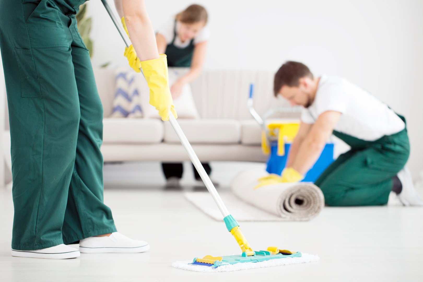Cleaner in green overalls cleaning floor using mop in the flat interior