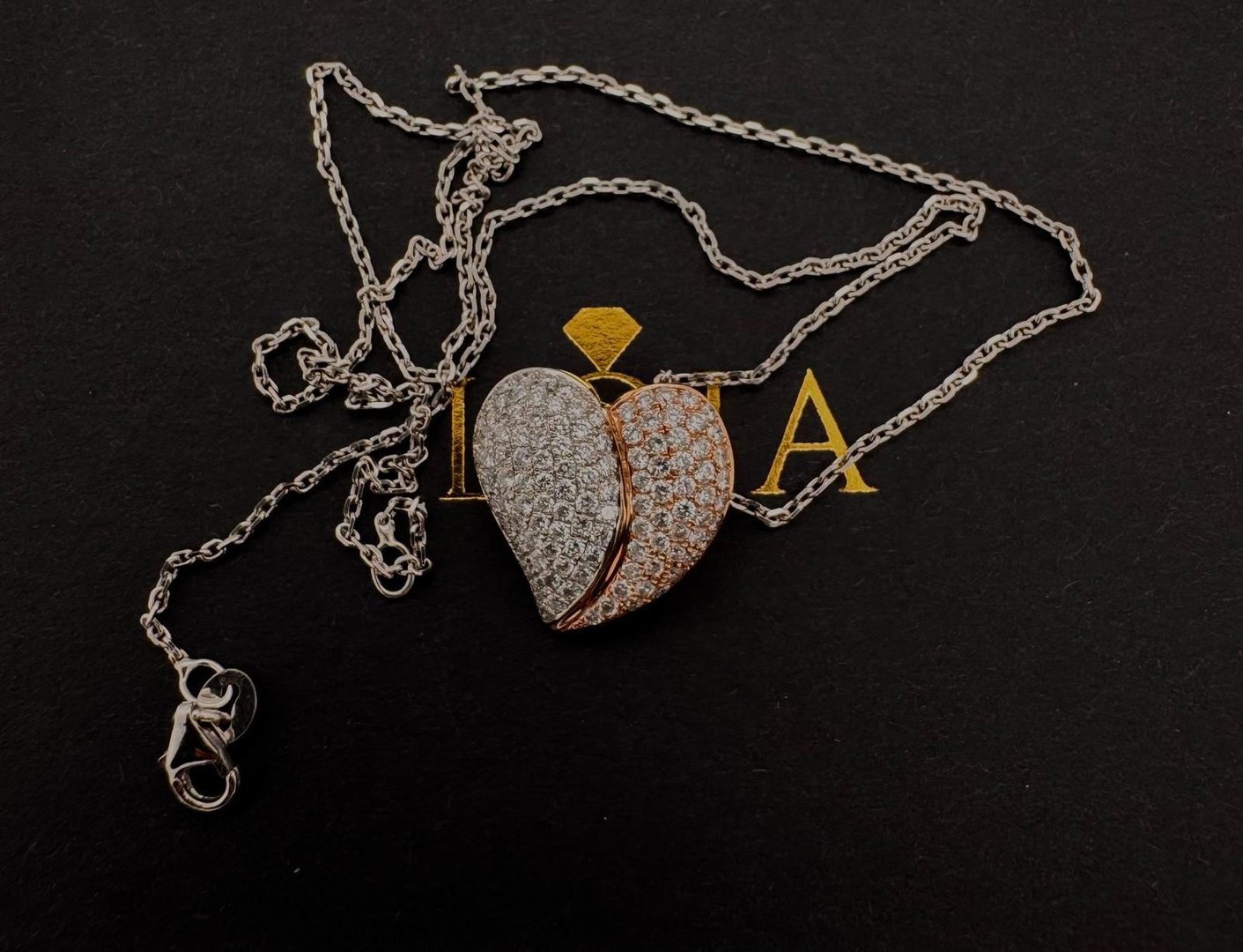 Heart-shaped pendant with silver and gold tones adorned with small crystals on a silver chain against a dark background.