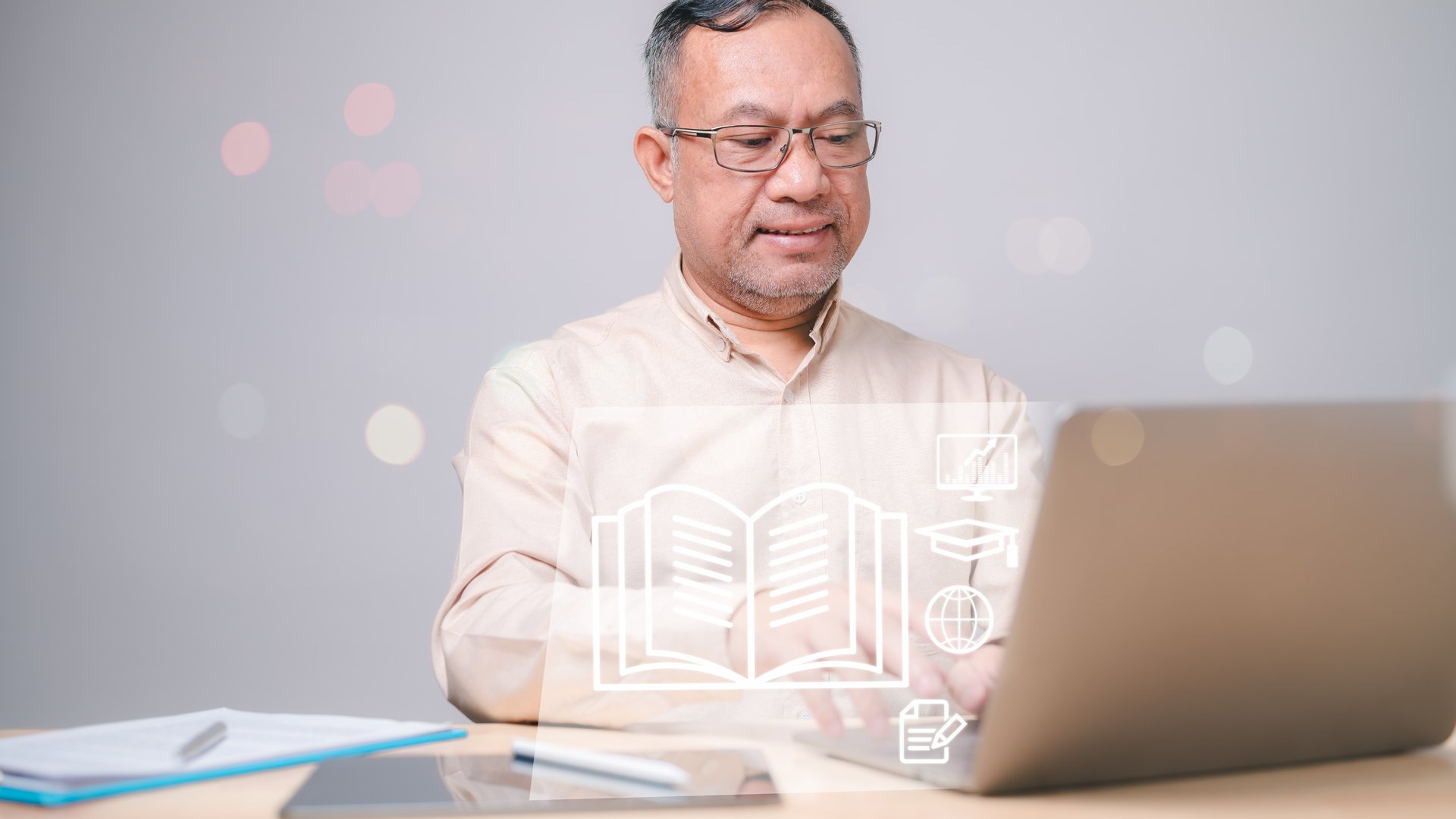 Adult Learning, An older man is sitting at desk with laptop open in front of him. Laptop screen shows an open book, and man is typing on it. Concept of Seniors in technology classes with laptop