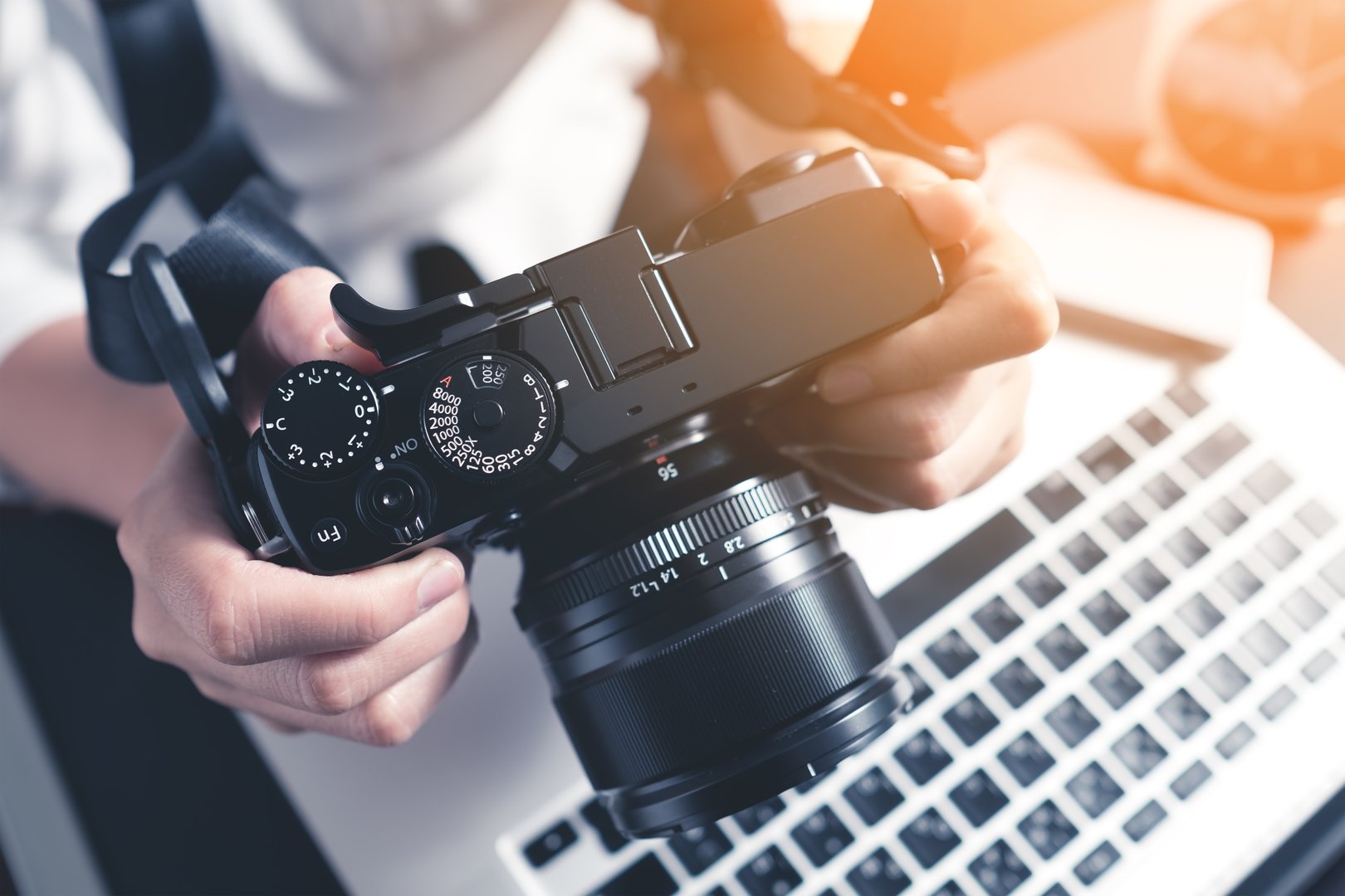Photographer holding camera on desk ready to  editing photos on laptop. Studio work, photo service concept. Workplace