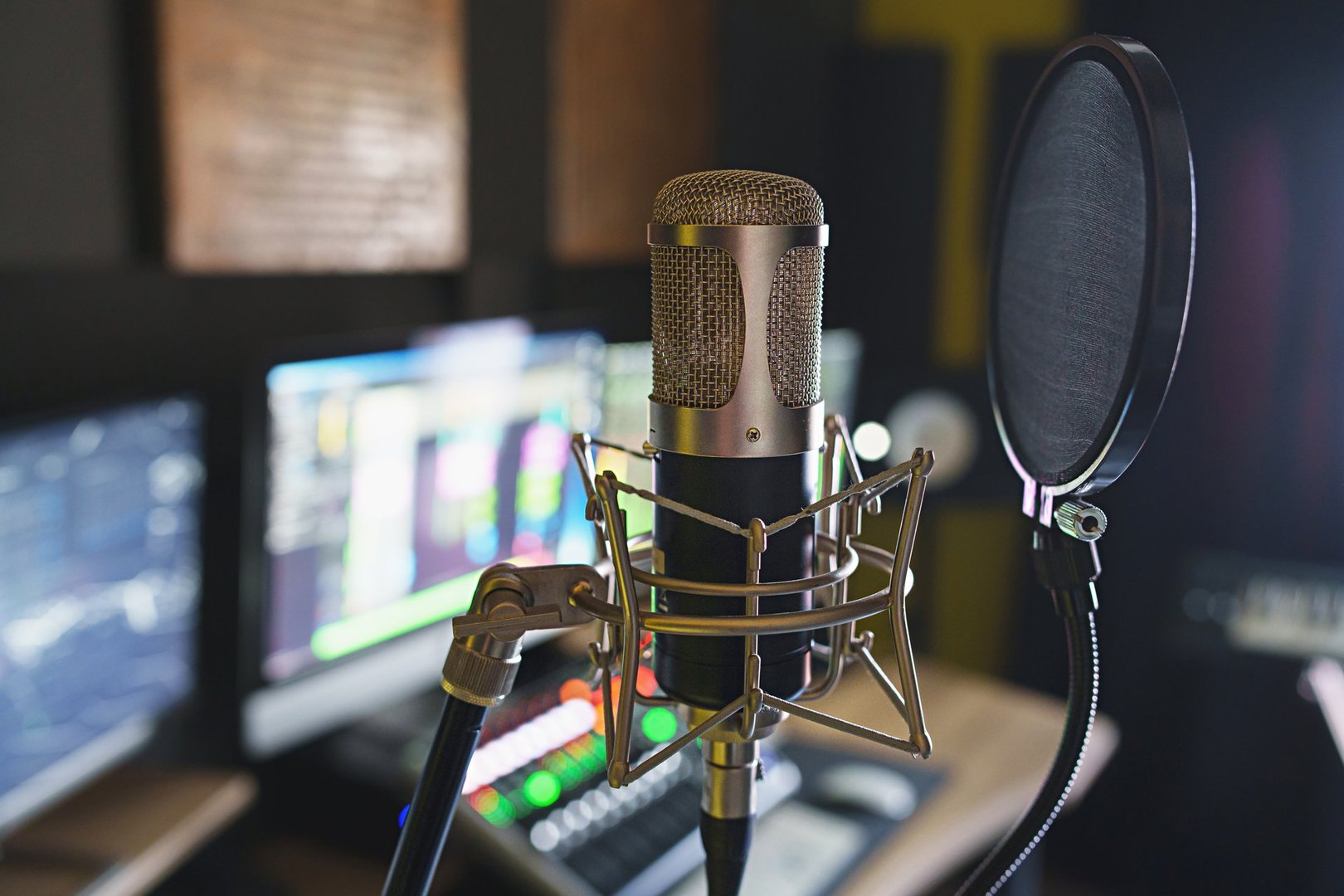 Close-up of microphone with blurred professional recording studio background, featuring mixer and monitor equipment.