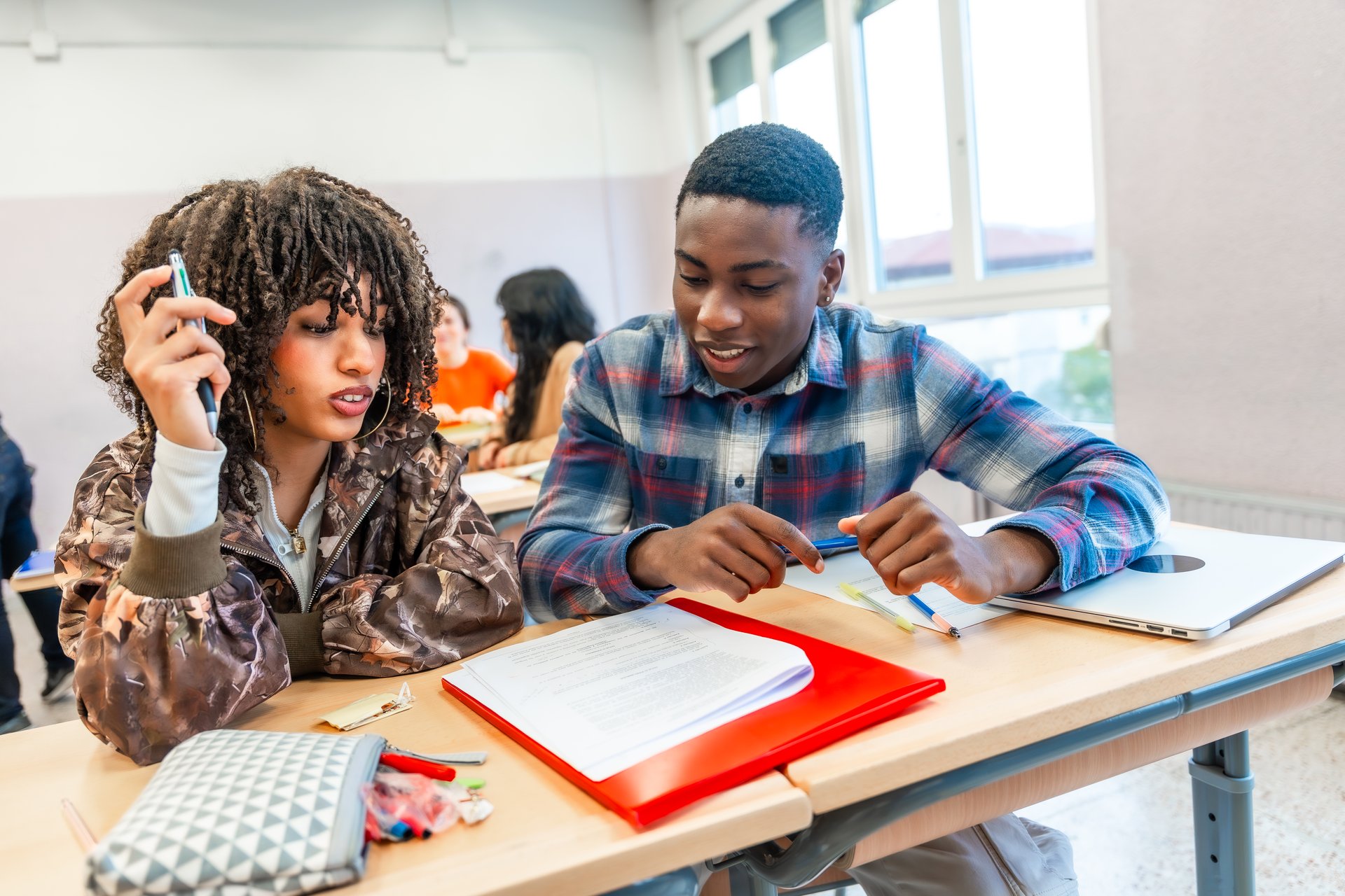 Two high school students are working together on a project, sharing ideas and discussing the task at hand in a classroom setting