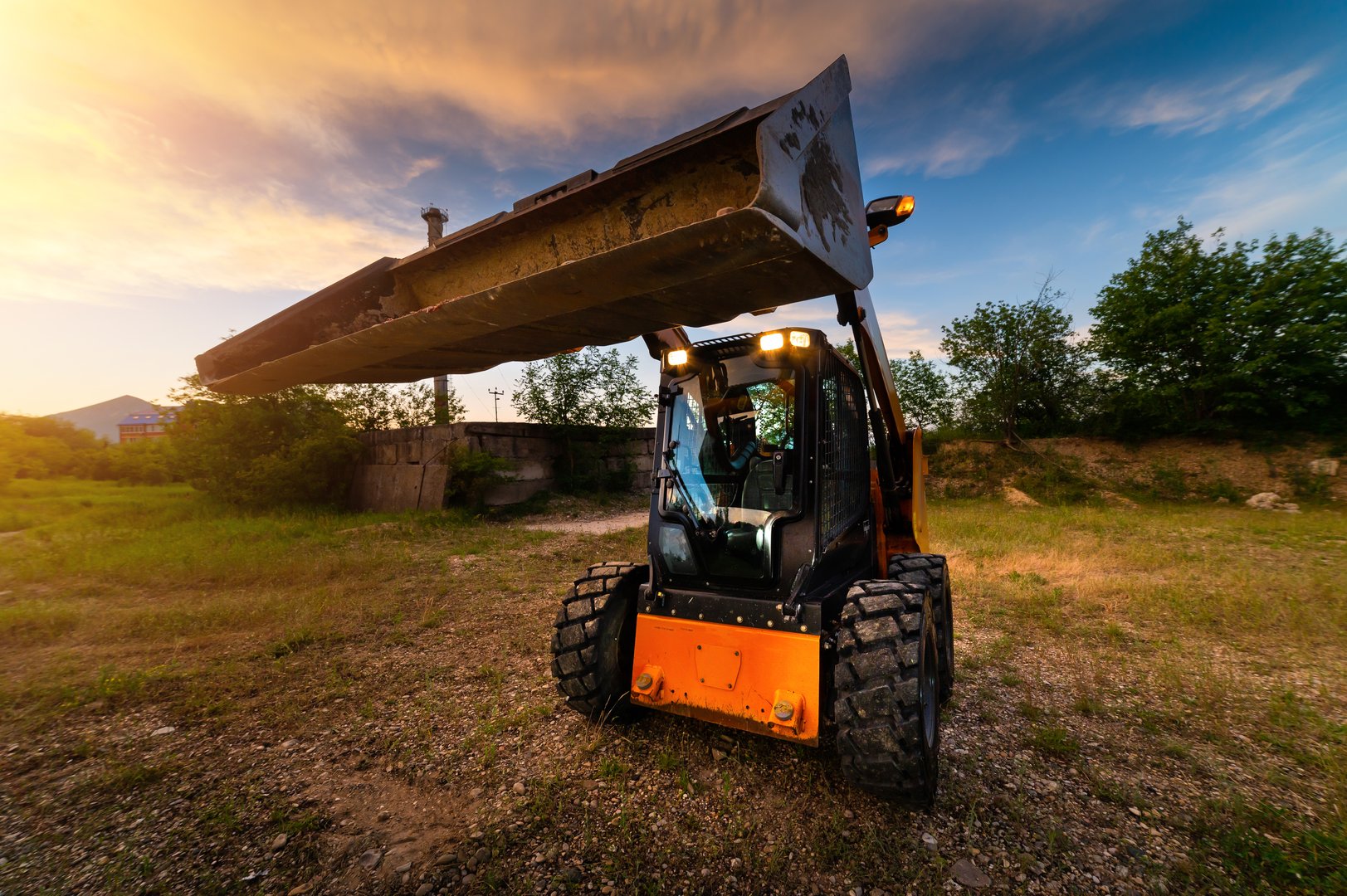 Mini bulldozer, small excavator against the backdrop of the sunset sky in the forest, wide angle.