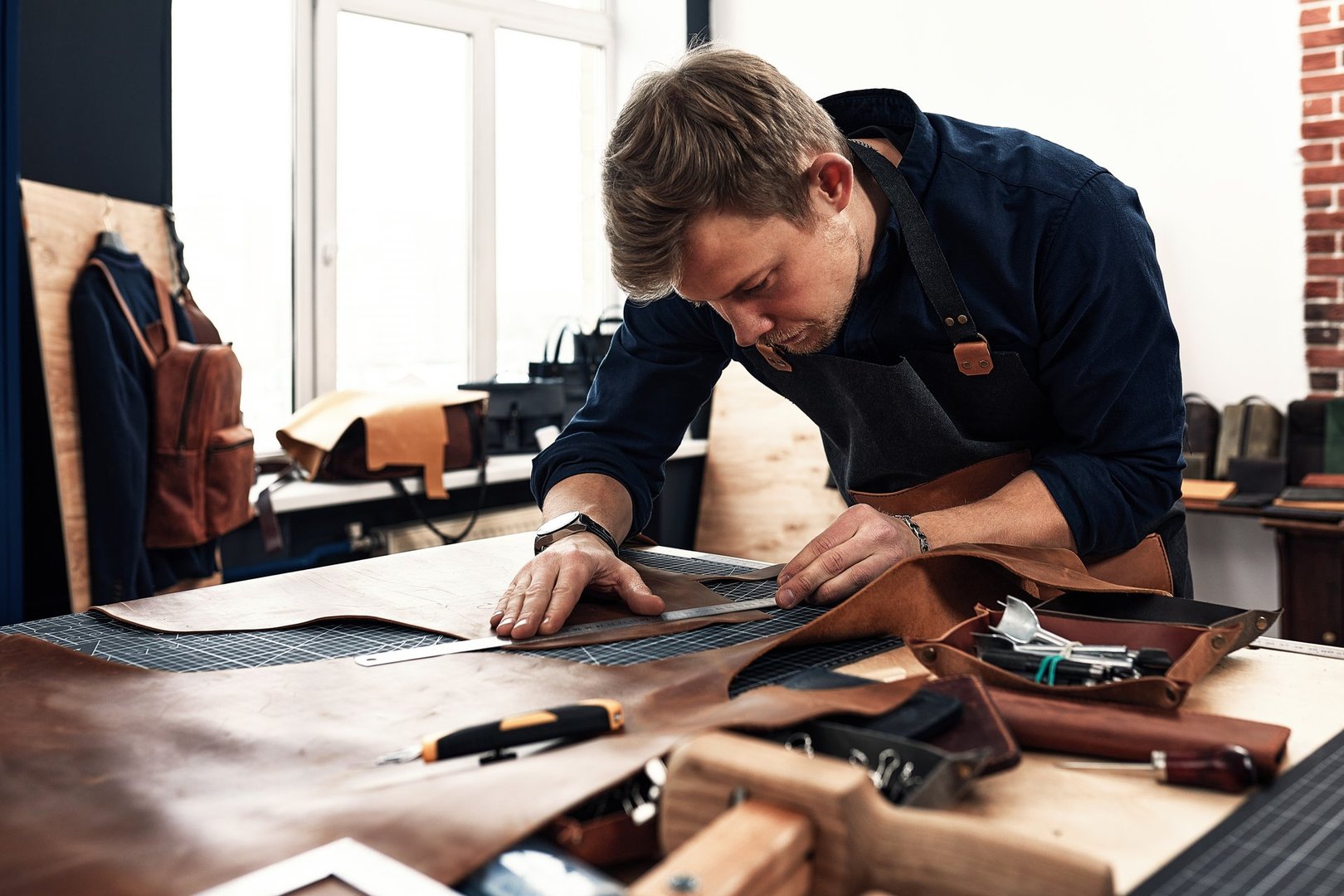 leather craftsmen working making measupenets in patterns at table in workshop studio.