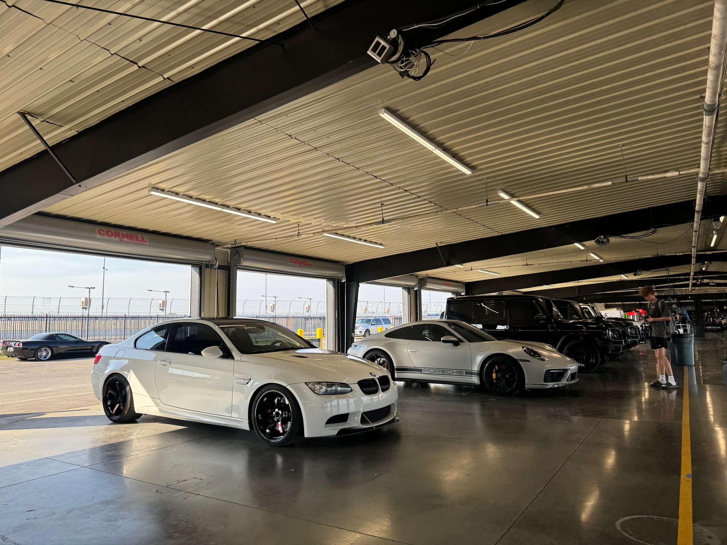 Clarksville, TN, USA - September 21, 2024: A white BMW M3 is parked in a garage. There are other cars in the background, including a Porsche 911 and several SUVs. The garage has fluorescent lights and a concrete floor.