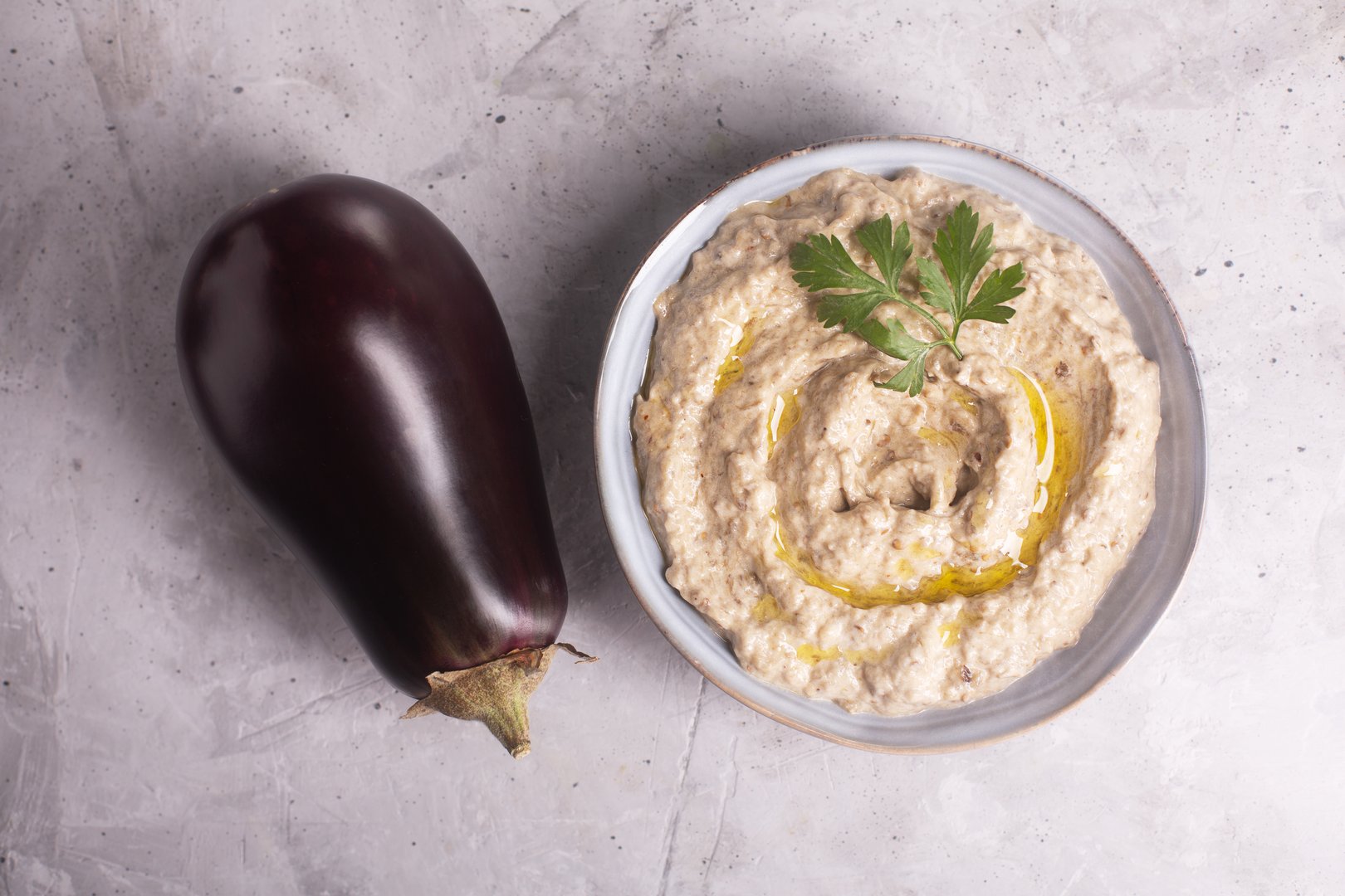 Baba ganoush Levantine cuisine appetizer of baked eggplant and sesame paste with herbs and olive oil on a concrete background