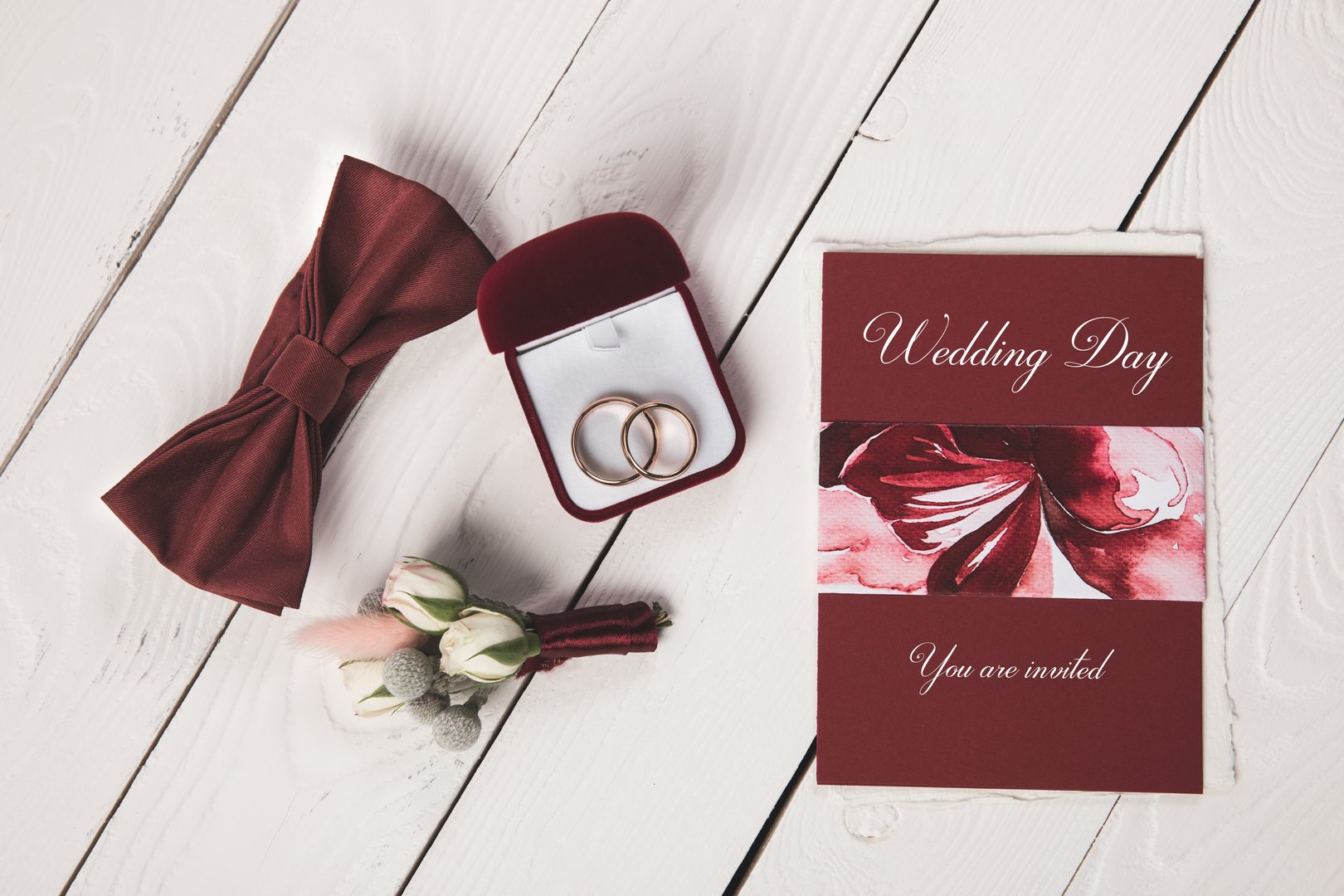 flat lay with invitation, buttonhole, bow tie and jewelry box on wooden tabletop