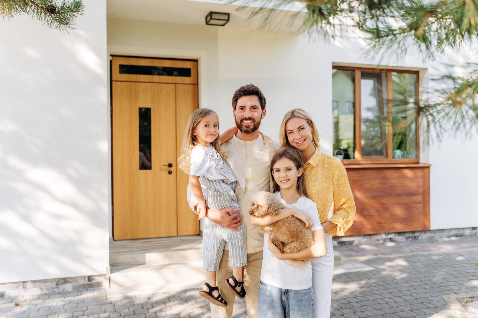 Smiling family with two daughters and small dog posing together in modern house looking at camera. Happy mother and father with little girls. Advertisement concept
