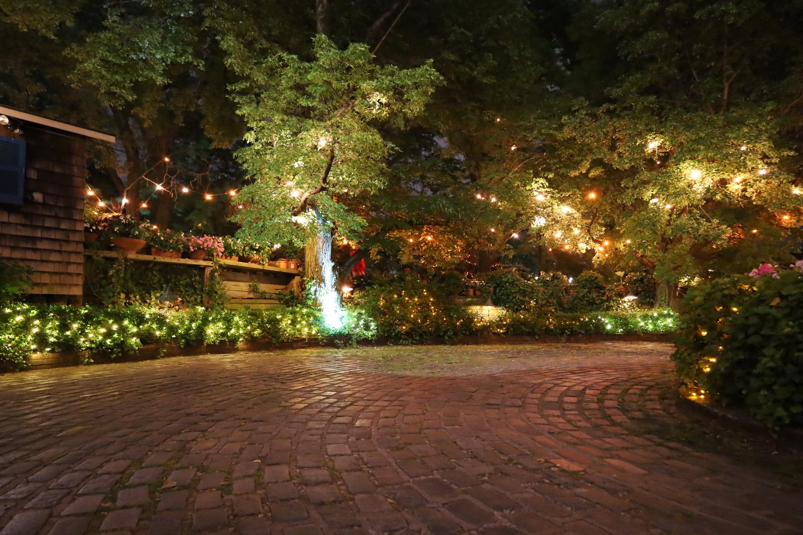 City Garden lighted on a hot summer night on the Brooklyn side of the East River, cottage, stone street, and pier, trees, lights, and colors.