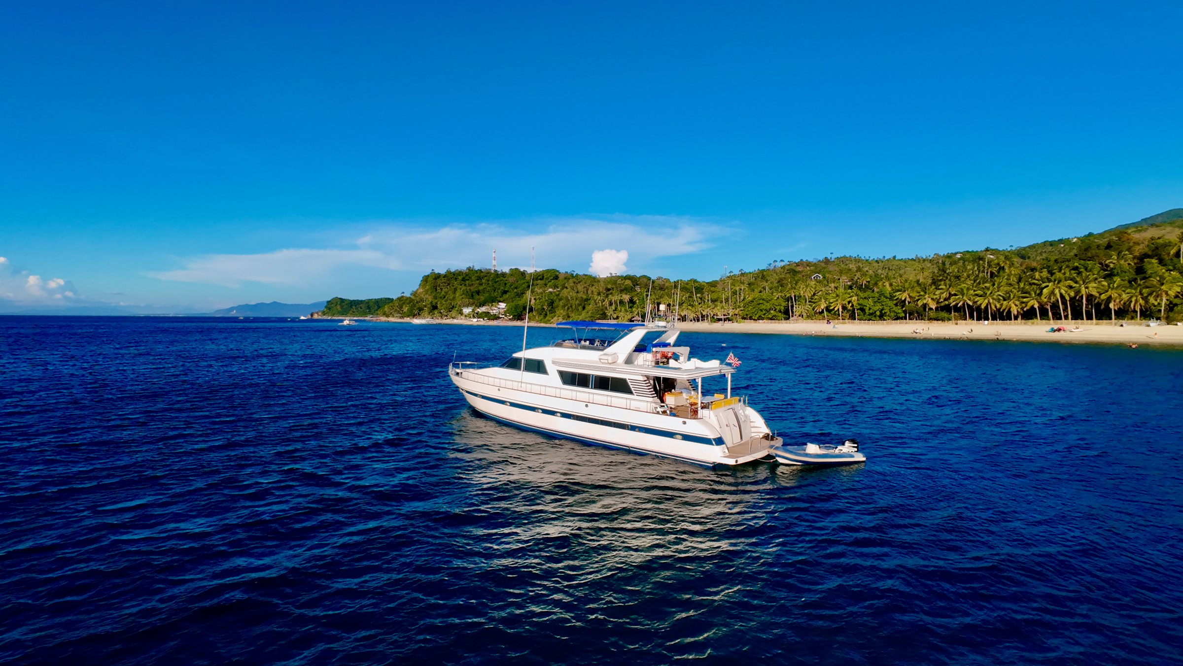 Aerial view of a white double-deck yacht parked in the sea opposite the coast of a tropical island.